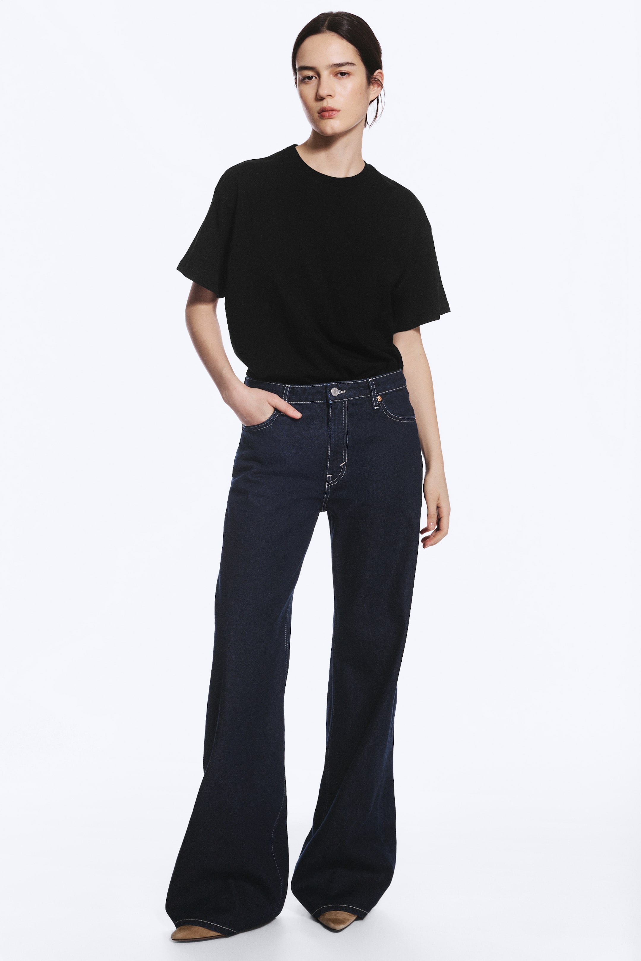 View larger image: A pair of dark wash, mid-rise, wide-leg jeans featuring light contrast stitching is being worn by the model. The jeans are styled with a tucked-in black T-shirt, and the model is standing with one hand resting in the front pocket.