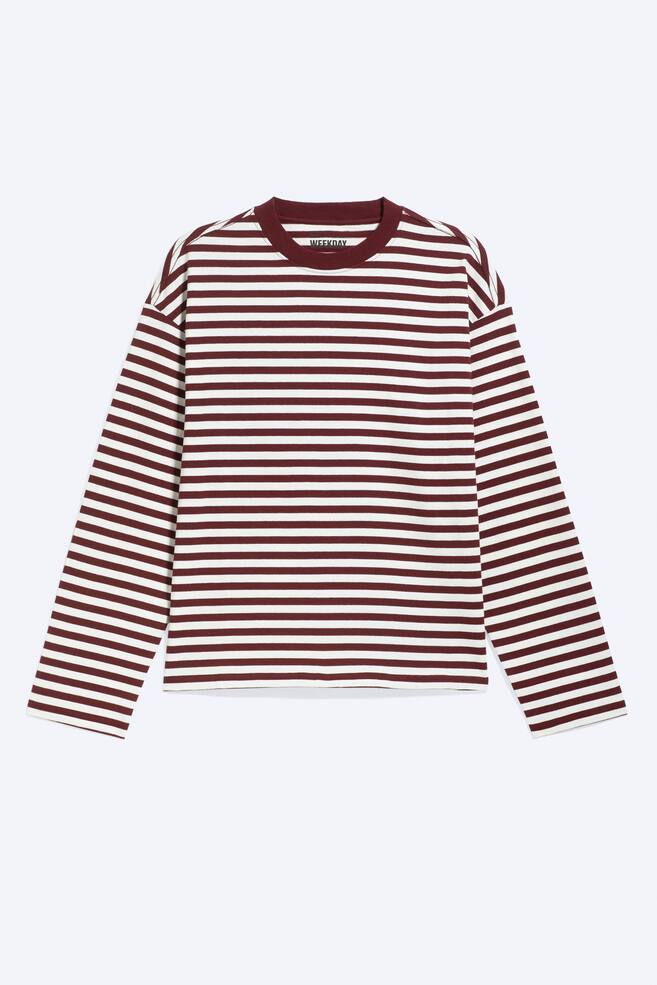 A boxy, long-sleeved T-shirt is shown from the front, featuring a horizontal burgundy and off-white striped pattern. The garment has a solid burgundy ribbed crew neck, dropped shoulders, and a straight hem. - 1