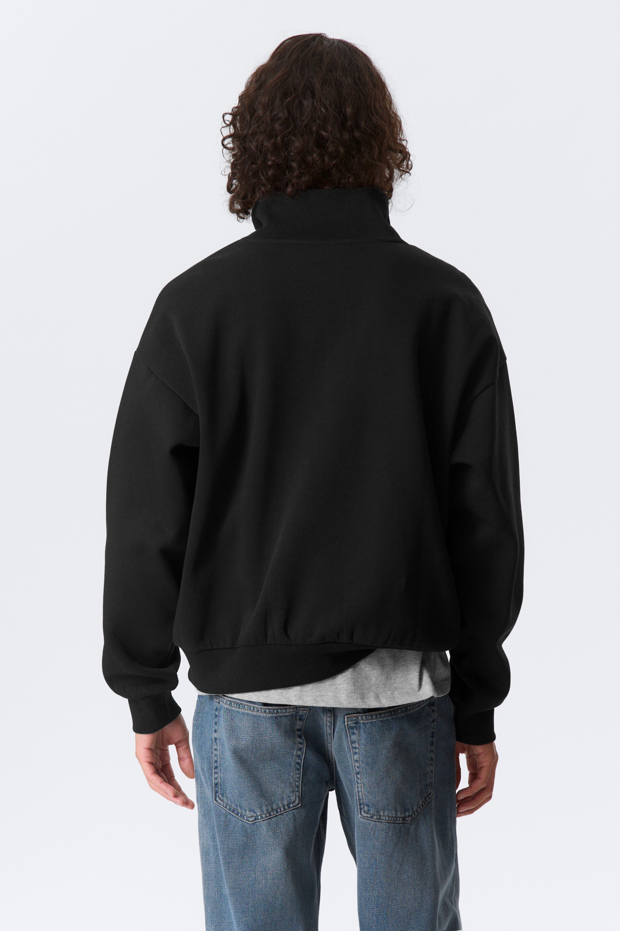 Ver imagen más grande: Una chaqueta negra de gran tamaño, con hombros caídos, un cuello alto, mangas largas con puños acanalados y un dobladillo acanalado, se está viendo desde atrás, con una camiseta gris visible debajo.