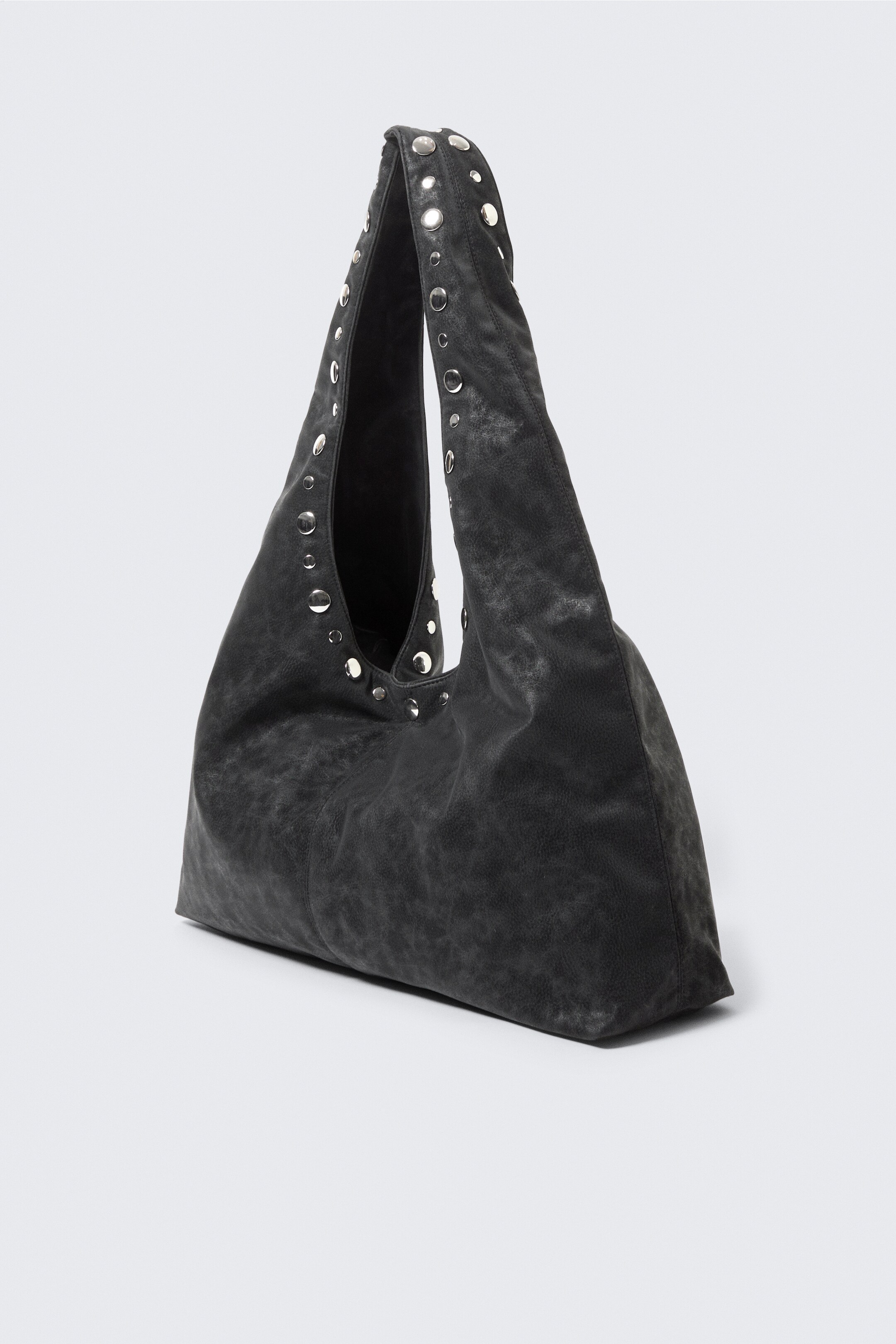 Agrandir l'image: Un sac à bandoulière gris foncé et décontracté présente une texture douce et usée semblable à du cuir et une silhouette triangulaire douce et sculpturale. Sa poignée supérieure incurvée est ornée de clous argentés le long des bords.