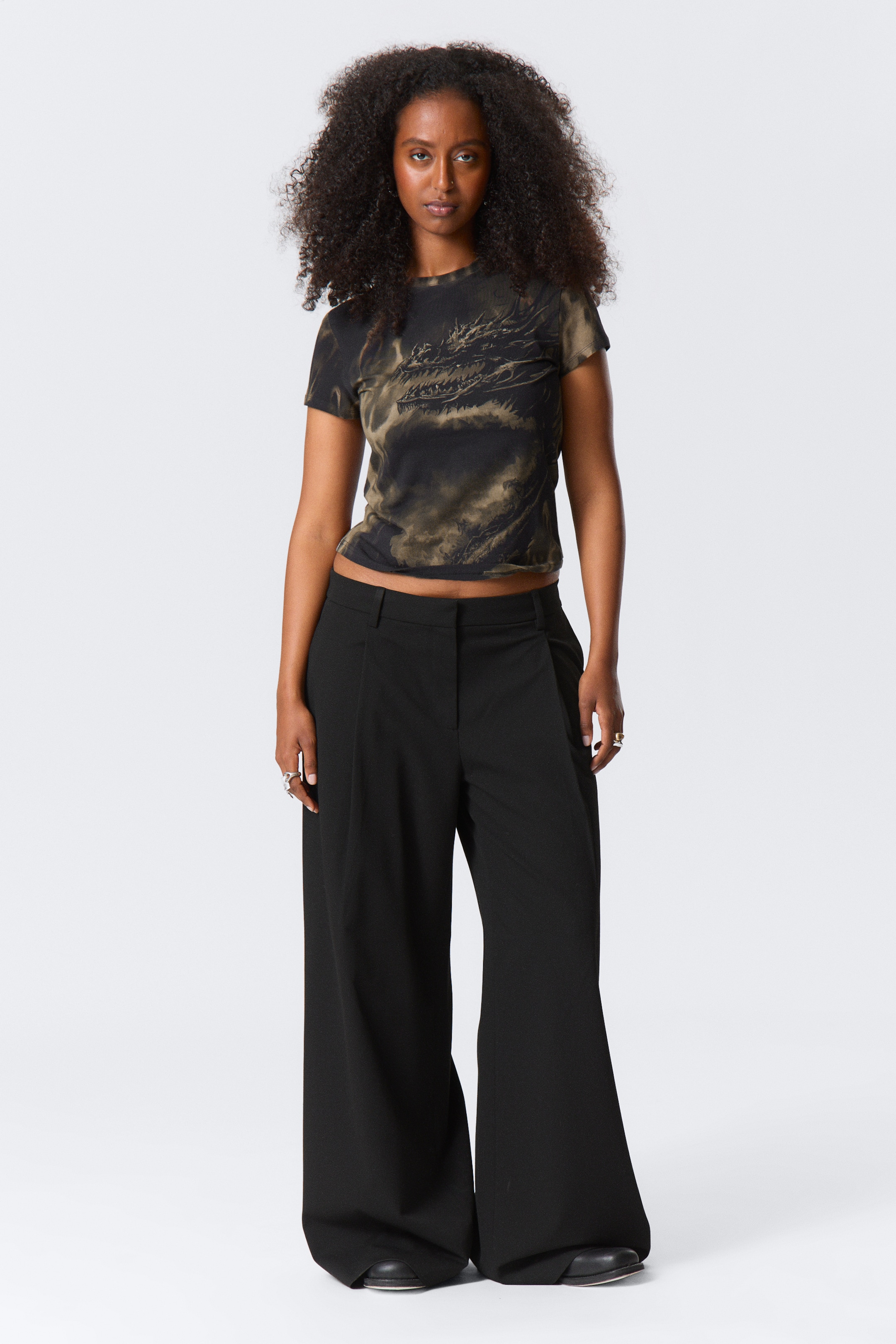 View larger image: A short-sleeved, black and greenish-brown tie-dye crop top, featuring a dark dragon graphic, is being worn. It is paired with black wide-leg trousers that are showing a relaxed fit and pooling at the ankles.