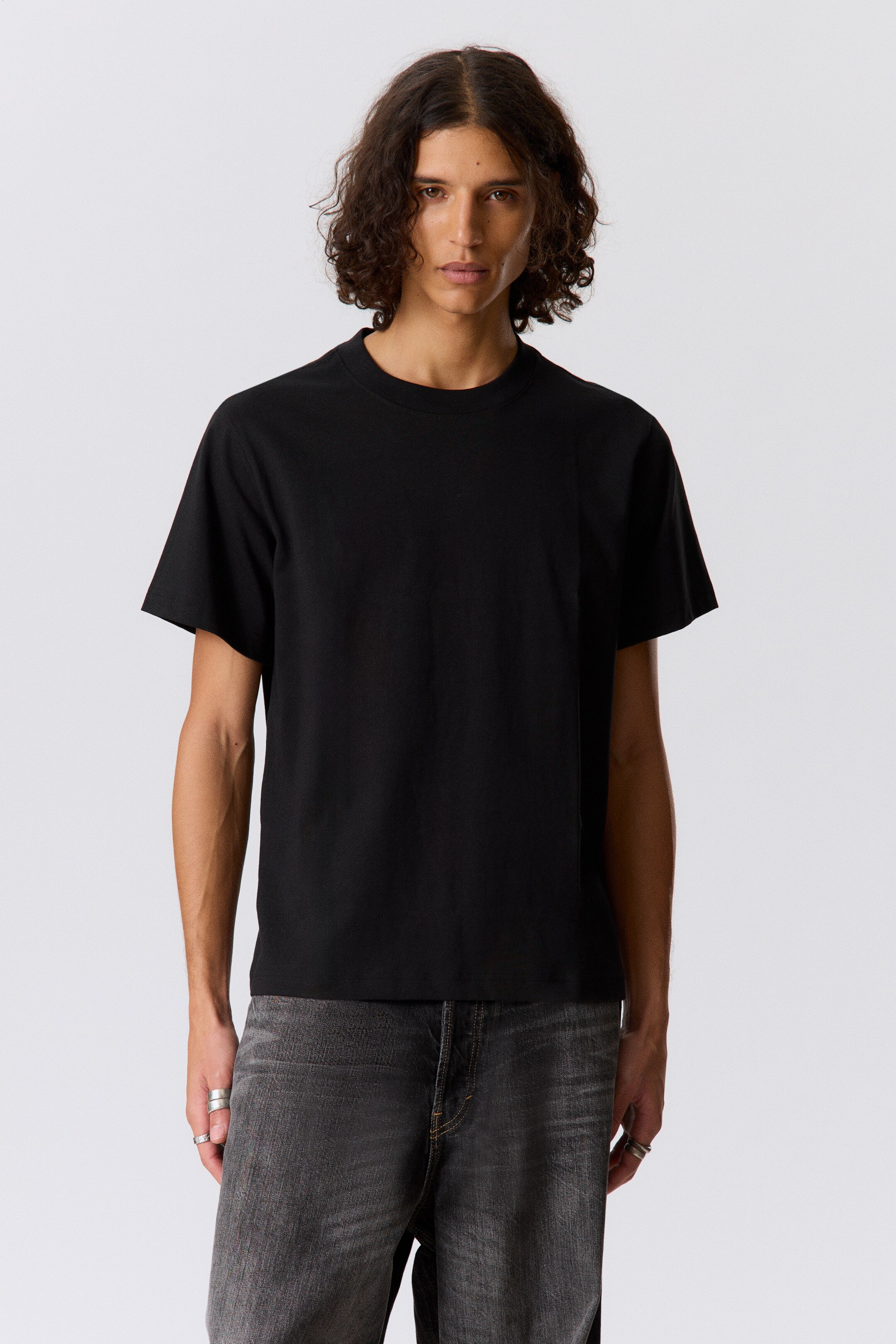 Ver imagem maior: Uma t-shirt preta de gola redonda está a ser usada, virada para a frente, com mangas curtas, um corte largo e uma bainha reta.