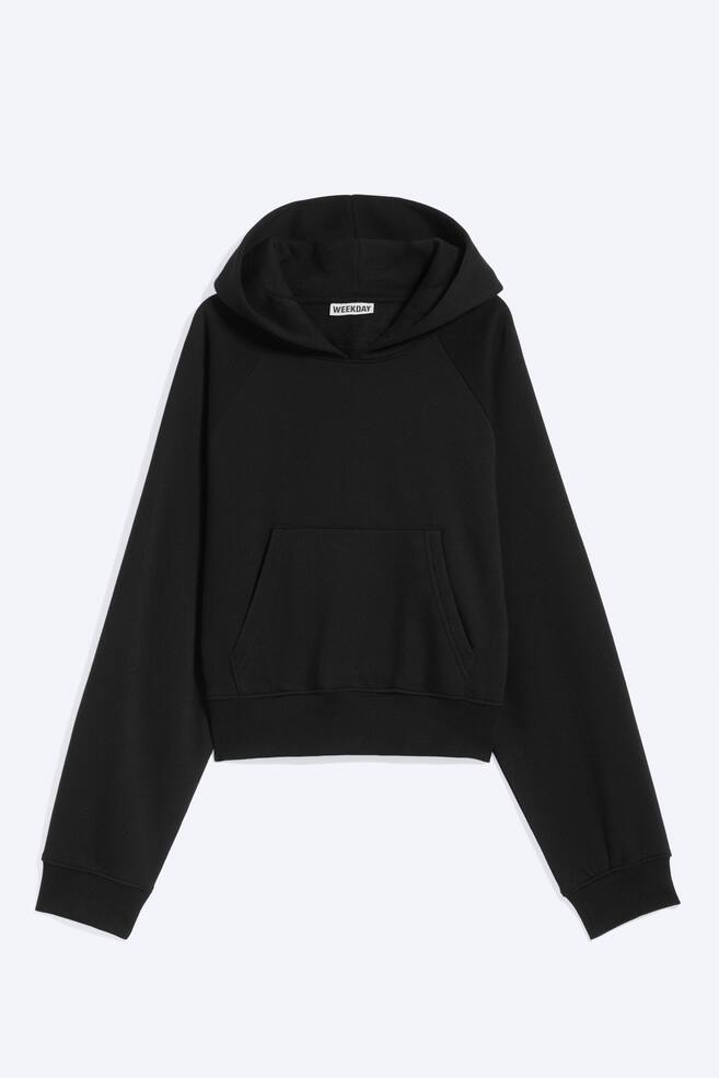 A black cropped hoodie is shown from the front, featuring a lined hood without drawstrings, raglan sleeves, and a front kangaroo pocket. The garment has ribbed cuffs and a matching ribbed hem. - 1