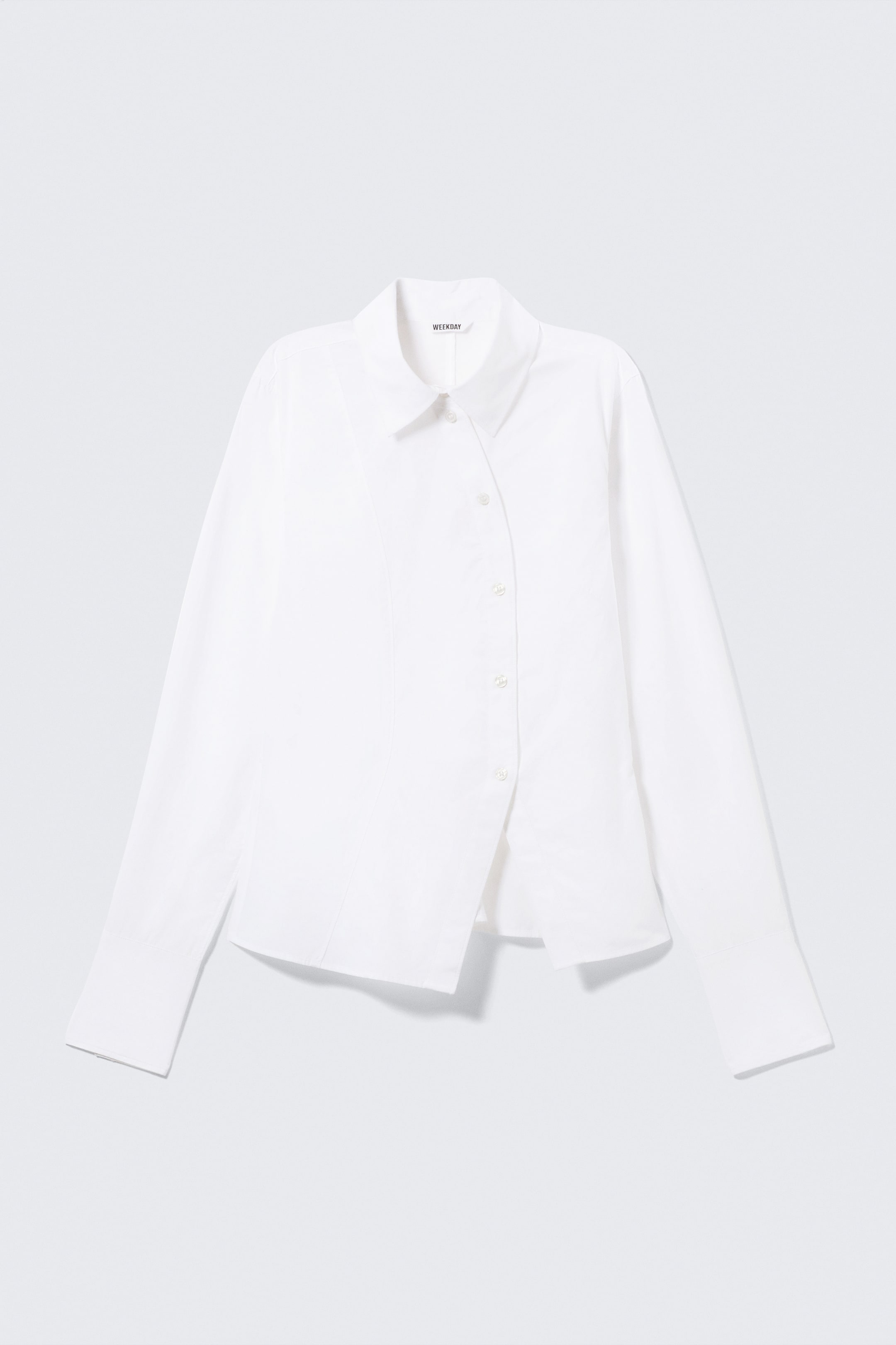 Grotere afbeelding bekijken: Het product is een wit overhemd met lange mouwen, gepresenteerd VOORAAN. Het is vervaardigd van frisse katoenen poplin en heeft een klassieke omgeslagen kraag en een gebogen knoopsluiting aan de voorkant. Zichtbare coupenaden vormen het lichaam voor een gestructureerde pasvorm, terwijl geplooide, geknoopte manchetten en een asymmetrische zoom de vormgeving compleet maken.