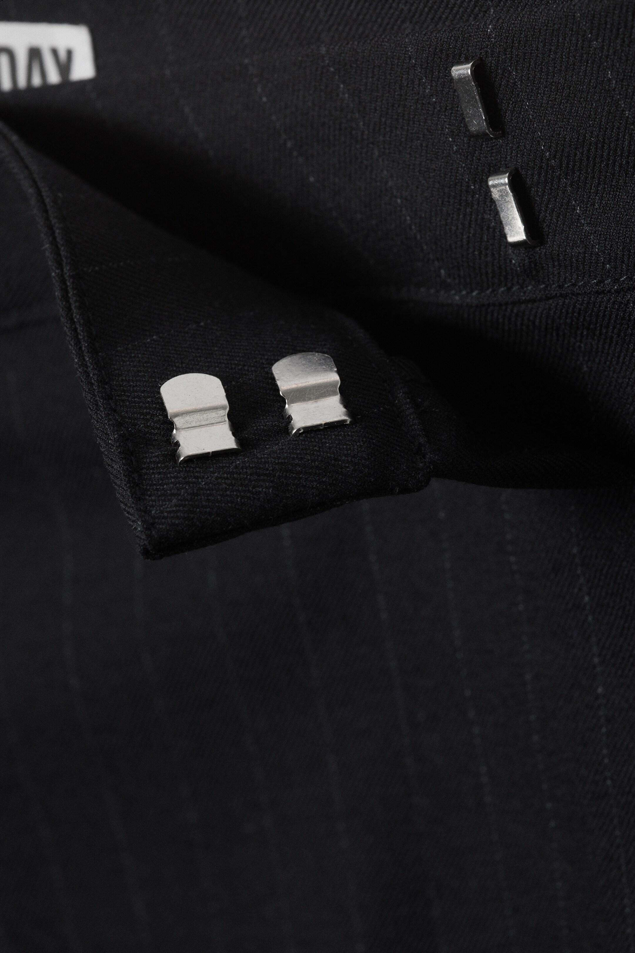 View larger image: The front closure of a dark, pinstriped garment is featuring two silver-toned hook-and-bar closures on a fabric tab, with two corresponding hooks visible on the main fabric.