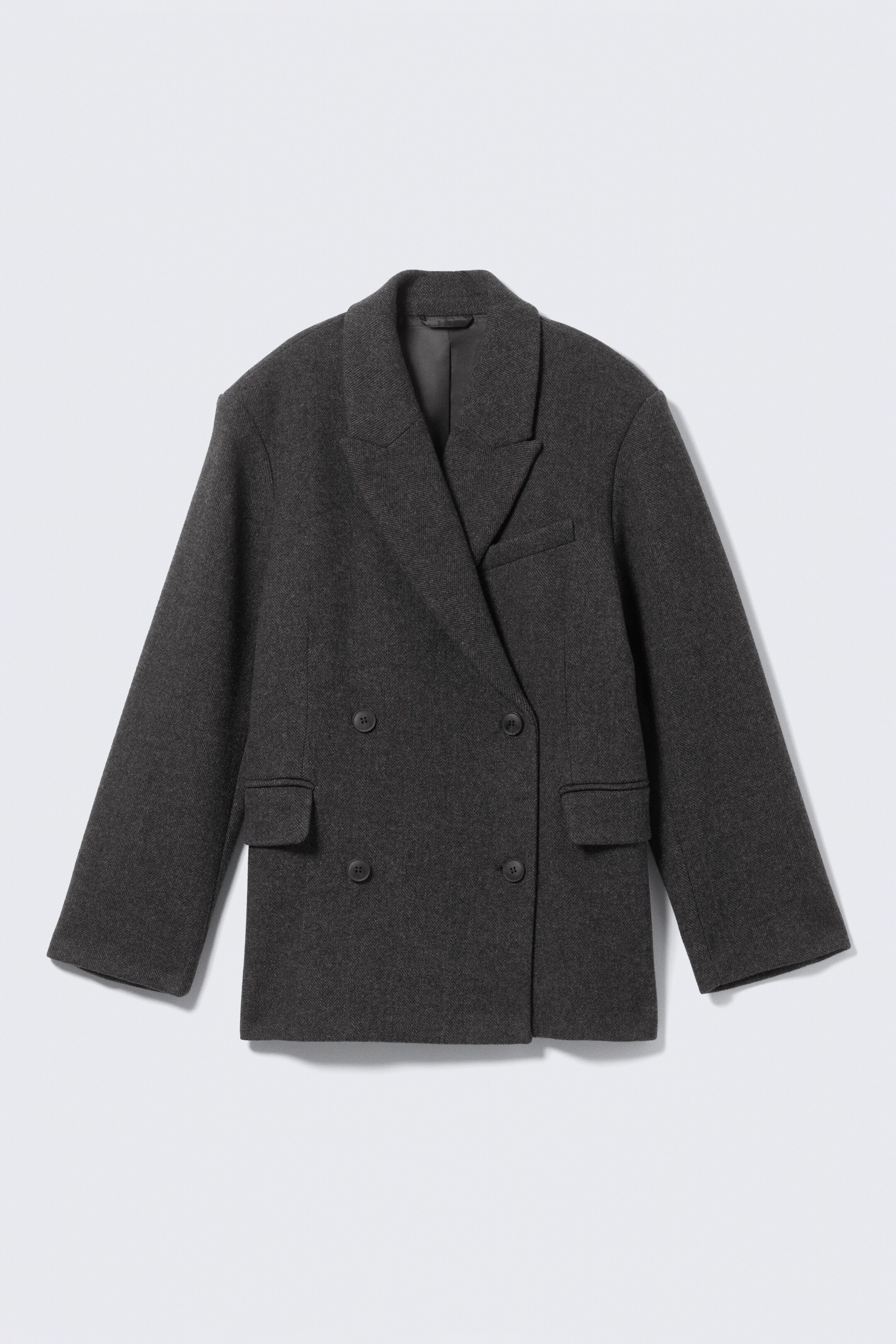 Größeres Bild ansehen: Ein dunkelgrauer übergroßer Blazer wird von vorne präsentiert, gefertigt aus einer strukturierten Wollmischung, mit scharfen Spitzfasson, einer doppelreihigen Vorderseite mit vier sichtbaren Knöpfen, einem horizontalen Leistentaschendetail auf der oberen linken Brust und zwei doppelt paspelierten Pattentaschen auf der unteren Vorderseite. Er zeigt einen sauberen, maßgeschneiderten Fall und einen geraden Saum.