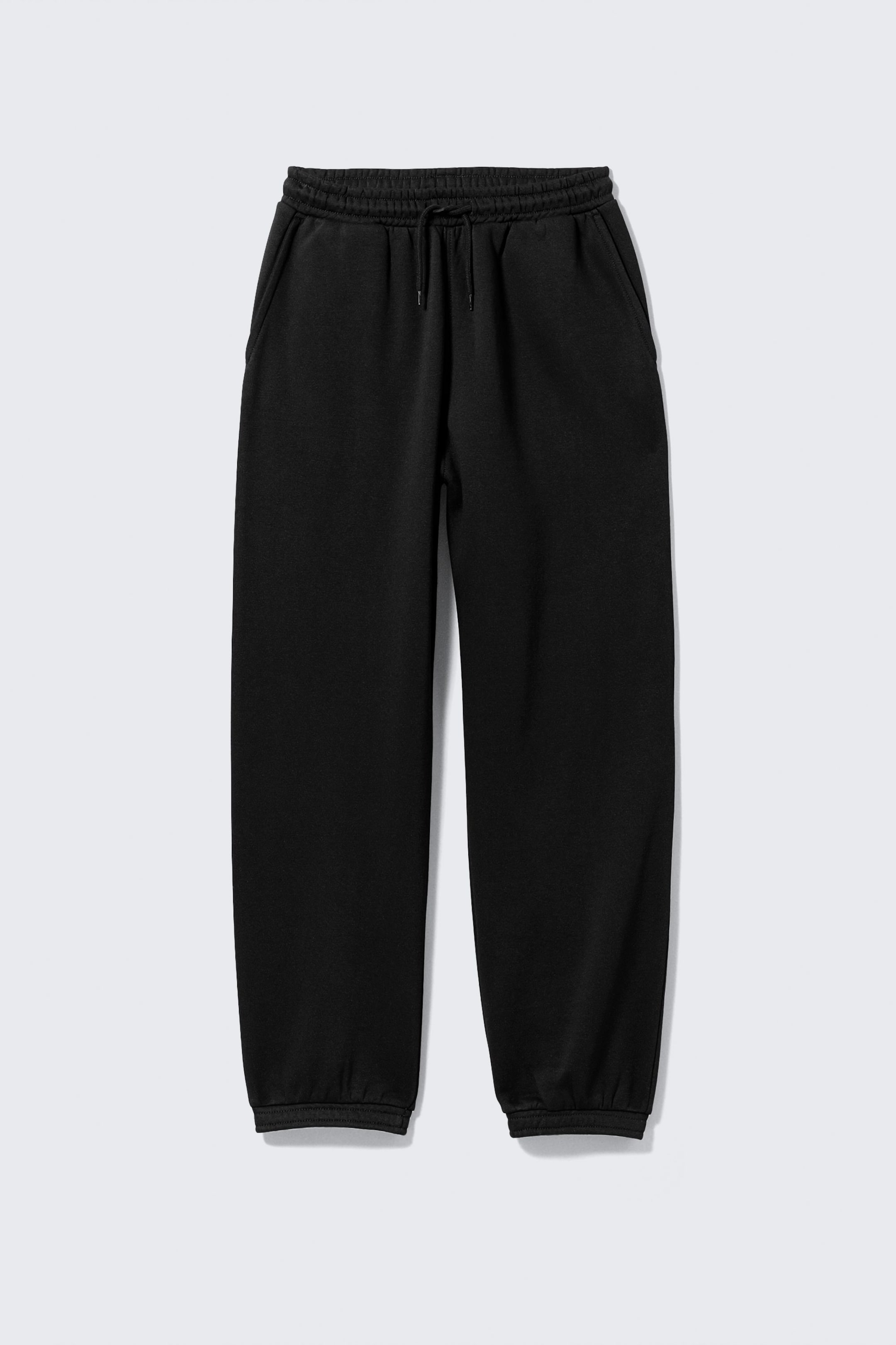 Agrandir l'image: Un pantalon de survêtement noir est présenté de face, avec une taille élastique dotée d'un cordon de serrage visible, deux poches latérales et des poignets côtelés aux chevilles.