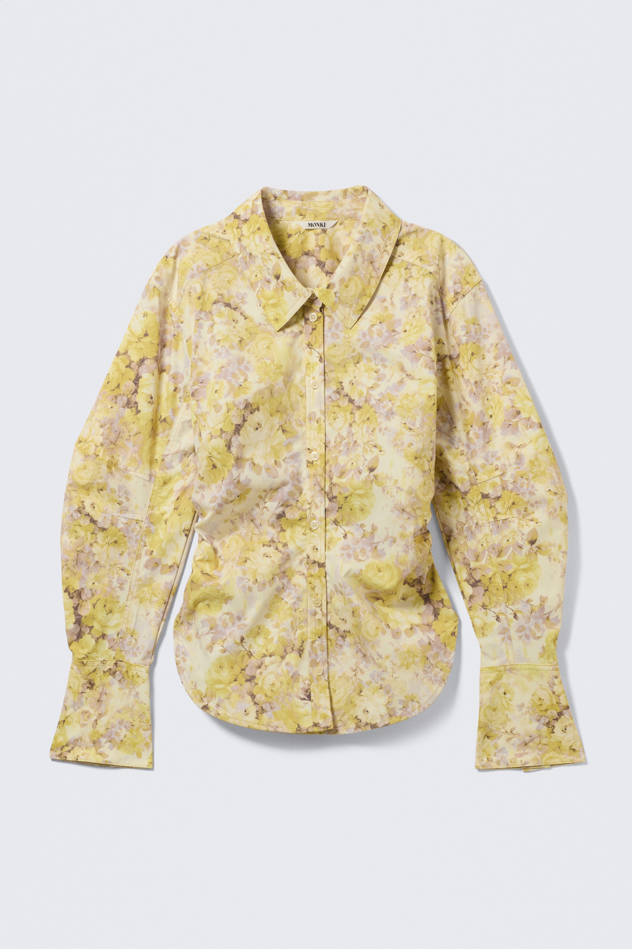 Visualizza l'immagine ingrandita: Una camicia giallo chiaro, con un motivo floreale in tonalità di giallo e lilla, è rivolta frontalmente. Presenta un colletto a punta con un'etichetta "MONKI" visibile, un'abbottonatura completa, maniche lunghe con polsini ampi a un bottone e un orlo leggermente curvato.