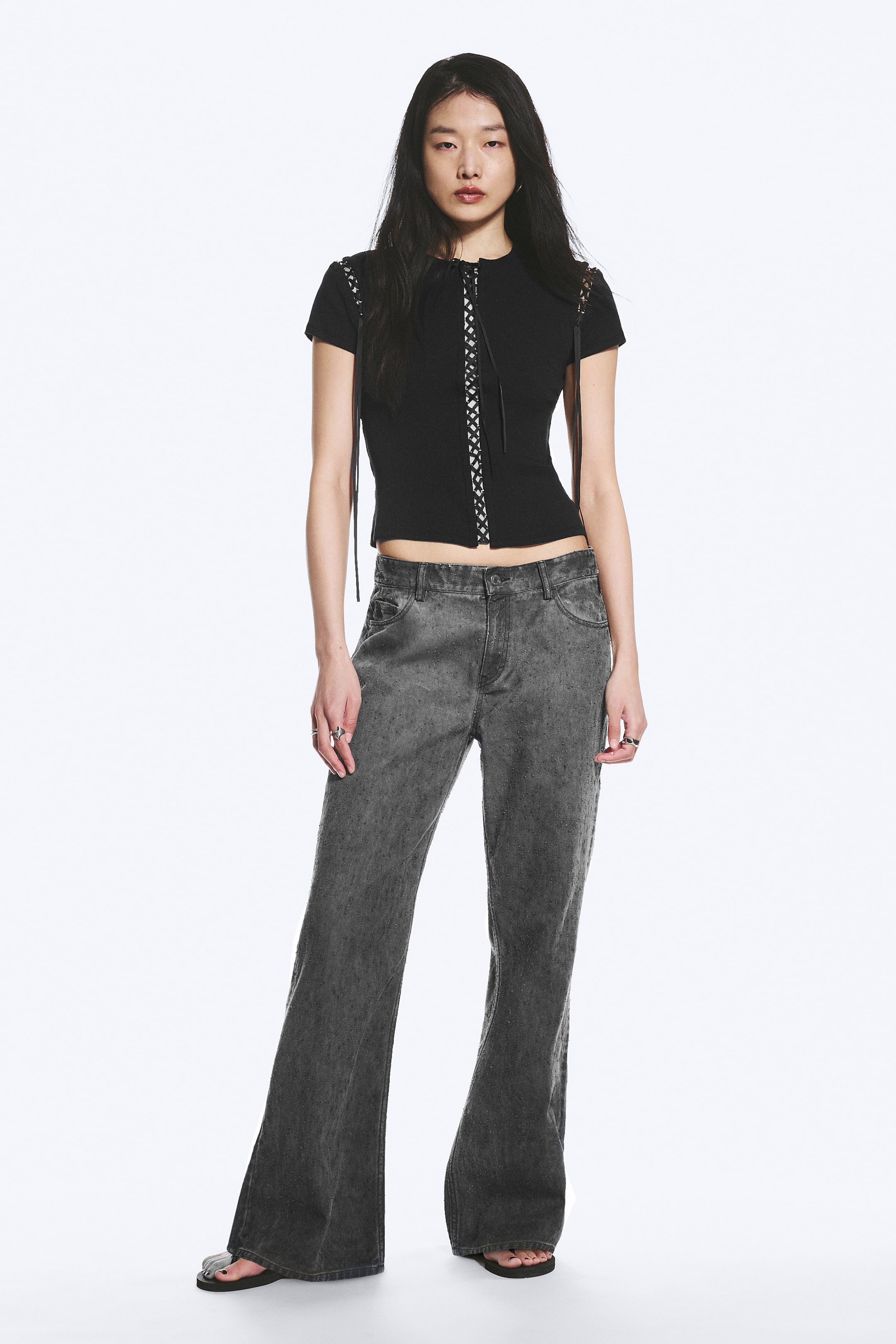 Se større billede: Et par grå, vasket bomuldsbukser med lav talje, løs pasform og bootcut-ben bæres af modellen. Bukserne har en klassisk fem-lomme konstruktion og lynlåsgylp med knaplukning.