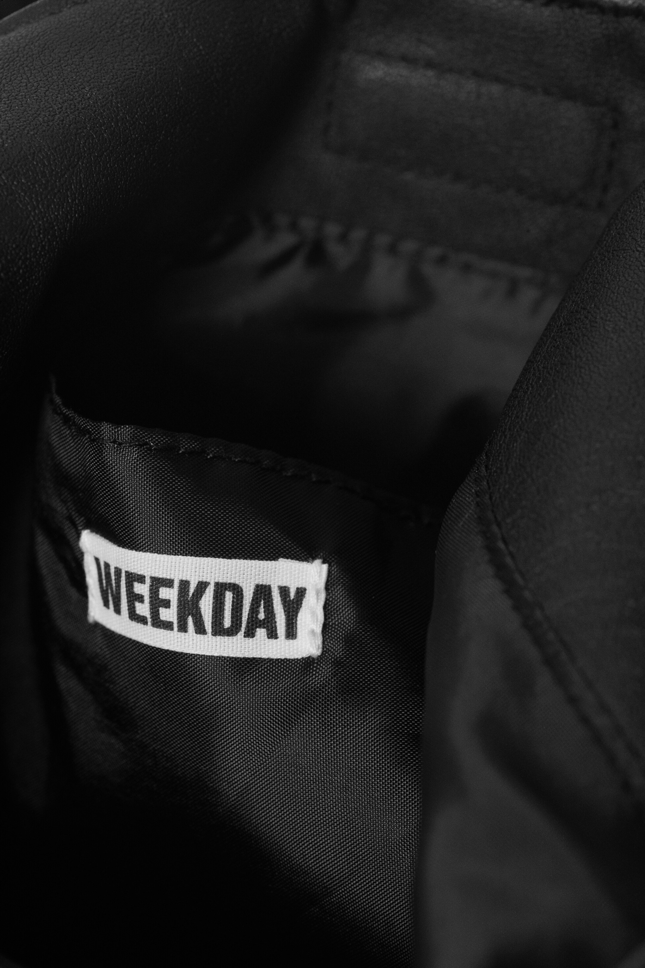 Grösseres Bild ansehen: Das Innere einer schwarzen Tasche ist sichtbar und zeigt eine Innentasche aus einem schwarzen gewebten Stoff. Ein weißes Stoffetikett mit „WEEKDAY“ in schwarzen Großbuchstaben ist an der Tasche befestigt.