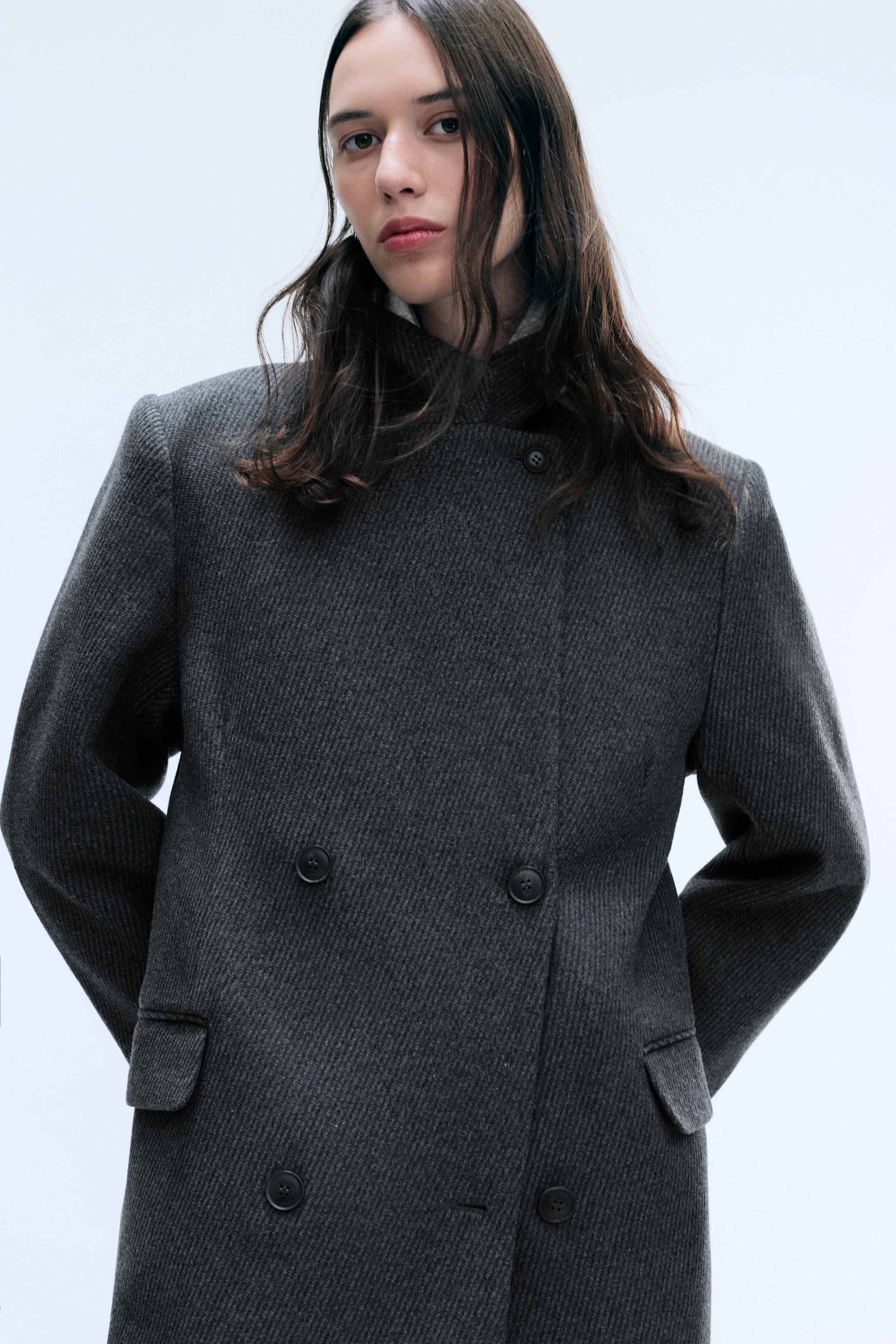 Visualizza immagine più grande: Il cappotto in misto lana Logan, a doppiopetto, in una tessitura testurizzata grigio scuro, è indossato dalla modella. Il cappotto presenta una chiusura con bottoni a collo alto, un fronte doppiopetto con bottoni scuri e tasche laterali con patta.