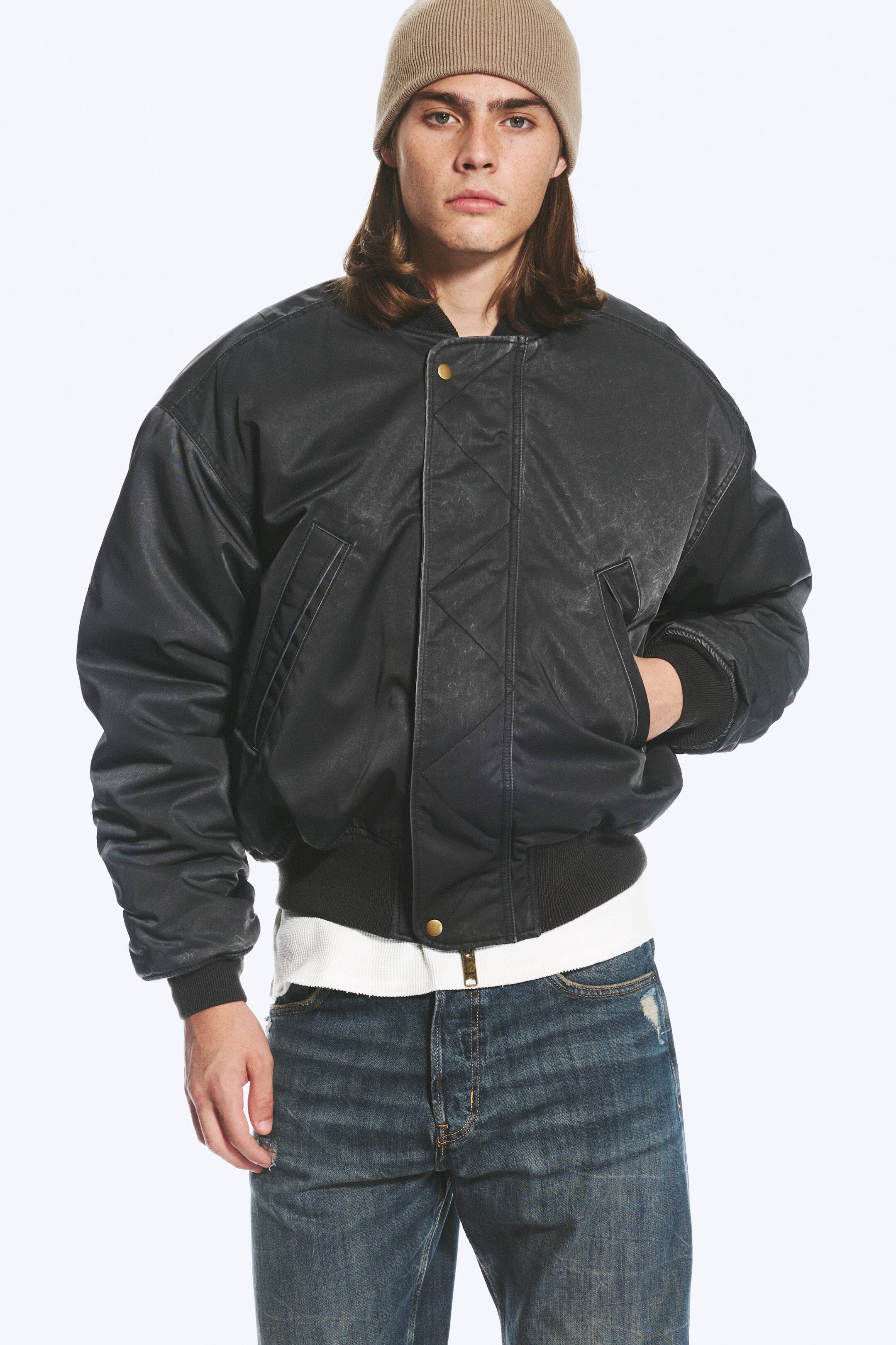View larger image: A relaxed bomber jacket in a faded black finish is worn by the model, who has one hand resting in the side pocket. The jacket features a quilted snap-button placket, along with a ribbed collar, cuffs and hem, and is layered over a white ribbed top and blue jeans.
