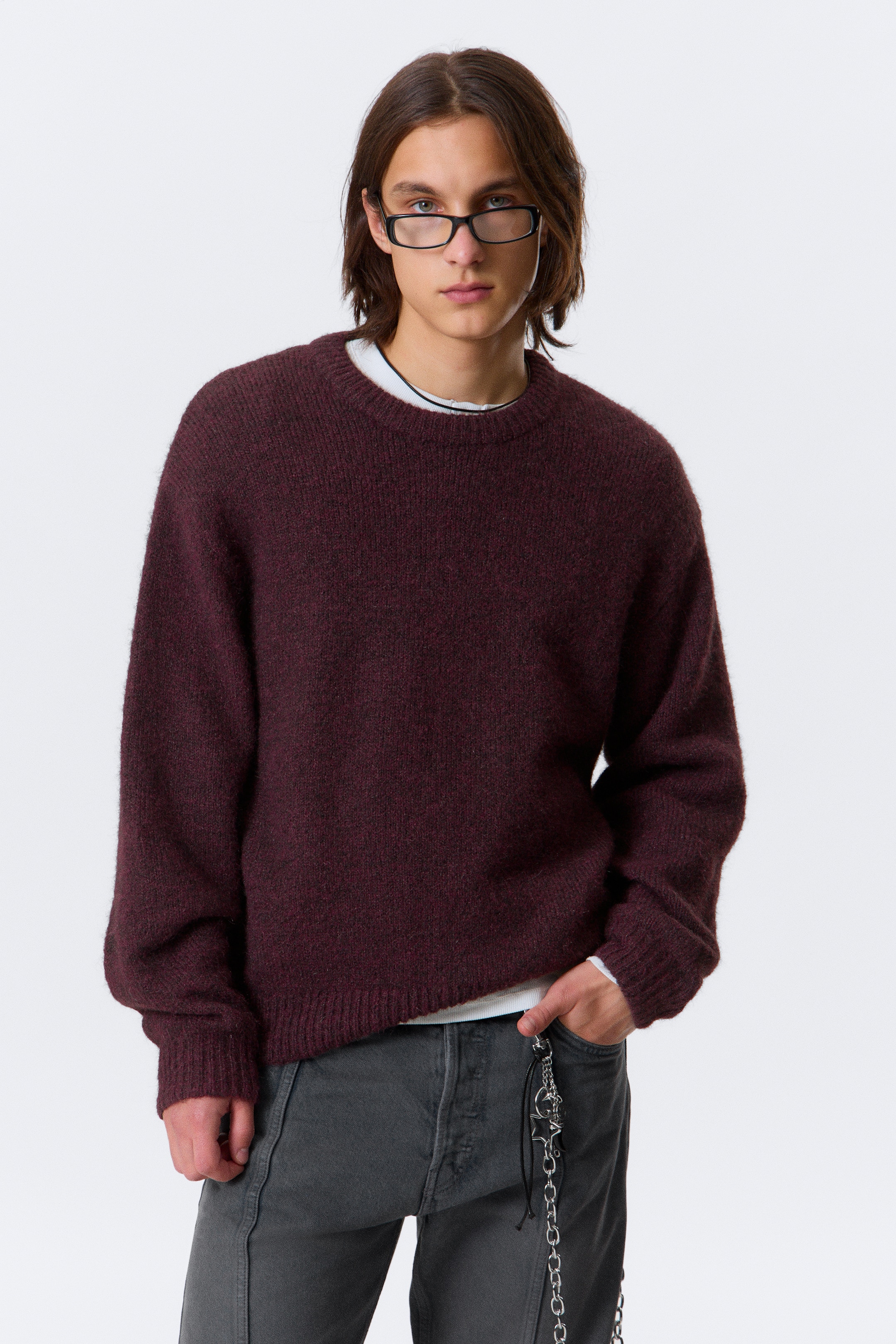 Visa större bild: En vinröd tröja med rund hals visas, med en avslappnad passform och en distinkt luddig stickad textur. Den har ribbade muddar, en ribbad fåll och en ribbad rund halsringning, med en vit t-shirt som subtilt lager under.