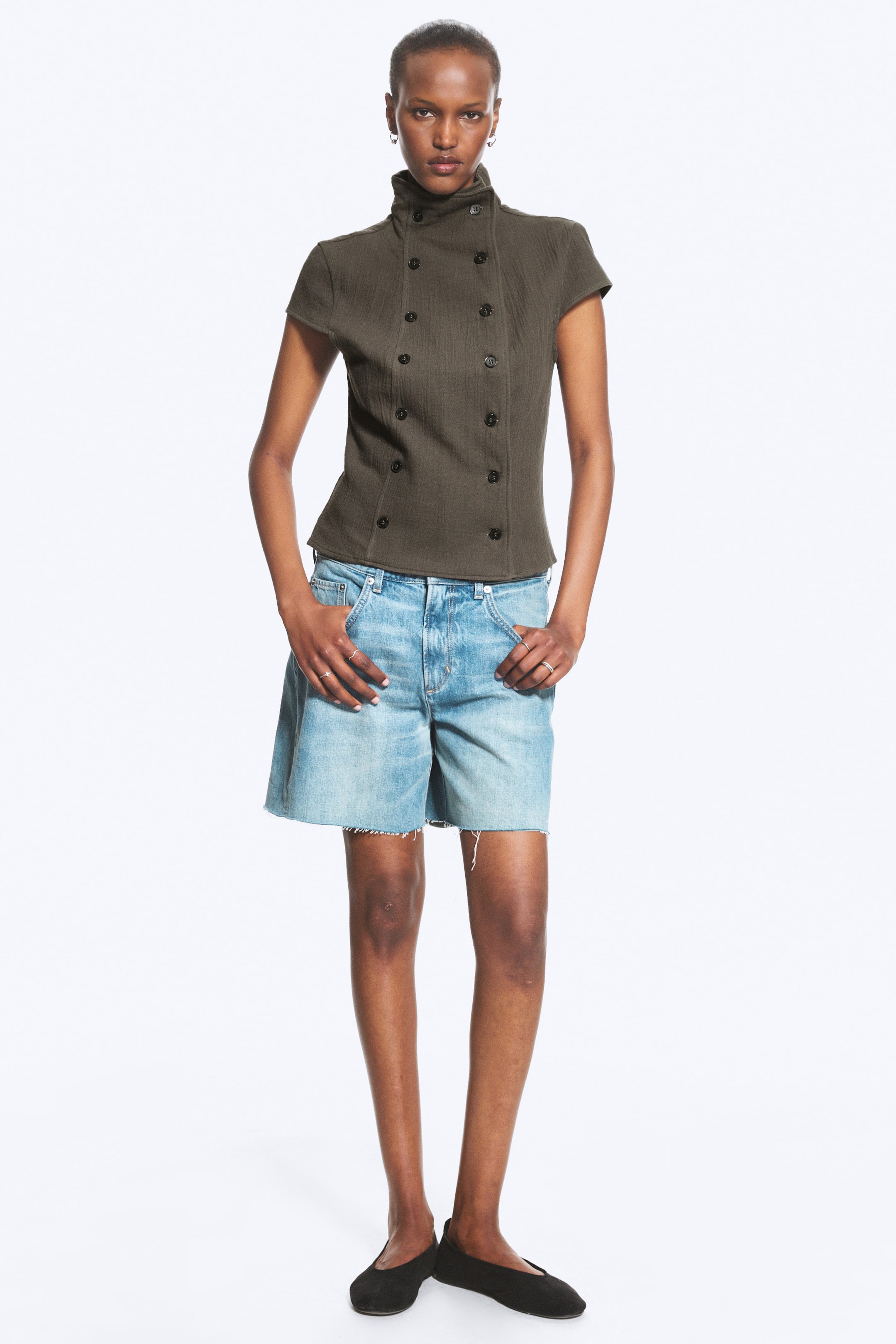 Visualizza immagine più grande: Top in Cotone Doppiopetto. Il top verde oliva, caratterizzato da un colletto alto e maniche corte, è indossato dalla modella. Presenta dodici bottoni scuri sul davanti doppiopetto.