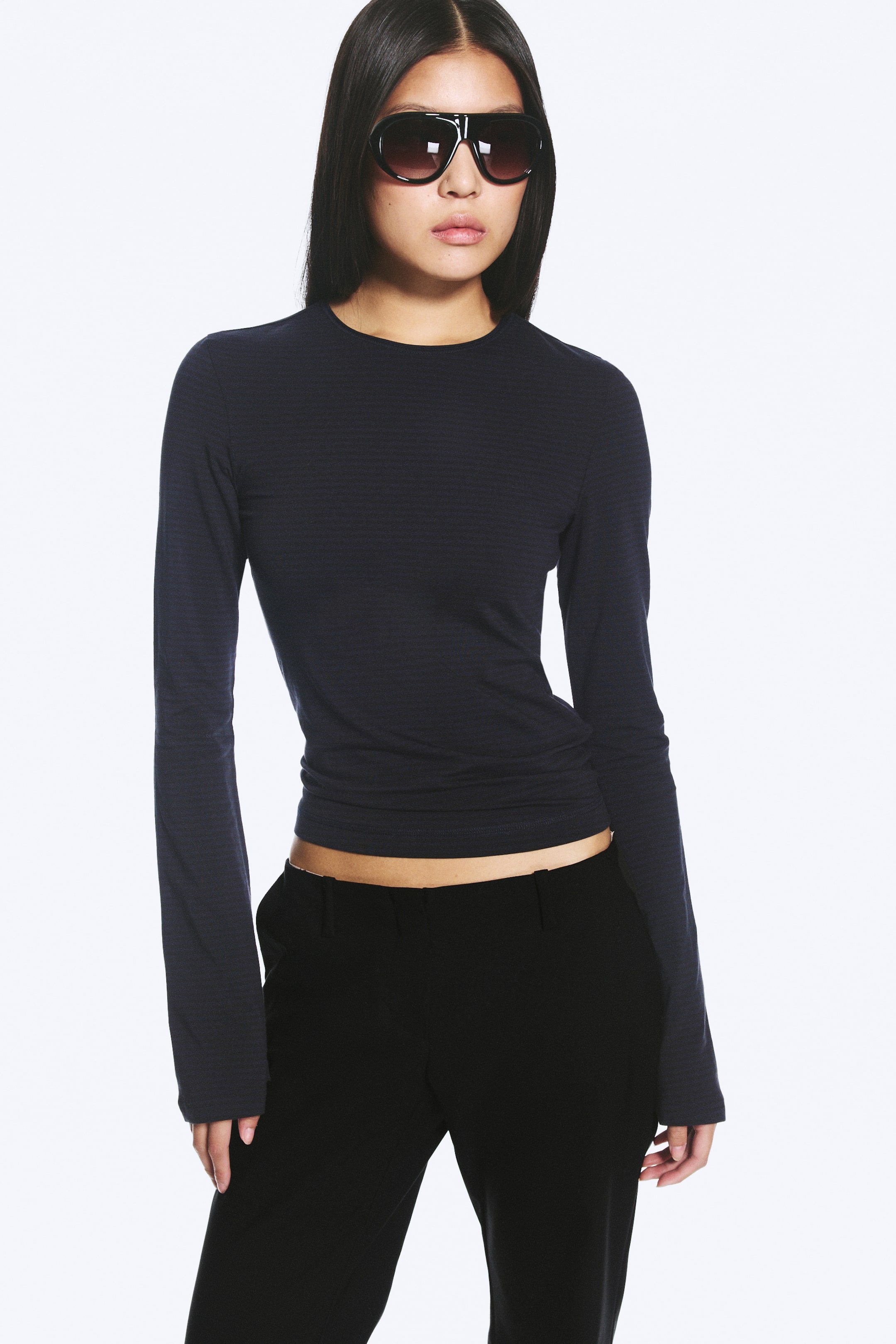 View larger image: A long-sleeved top with a subtle textured pattern, round neckline, and slightly fluted cuffs is being worn by the model, with its straight hem sitting above black trousers.