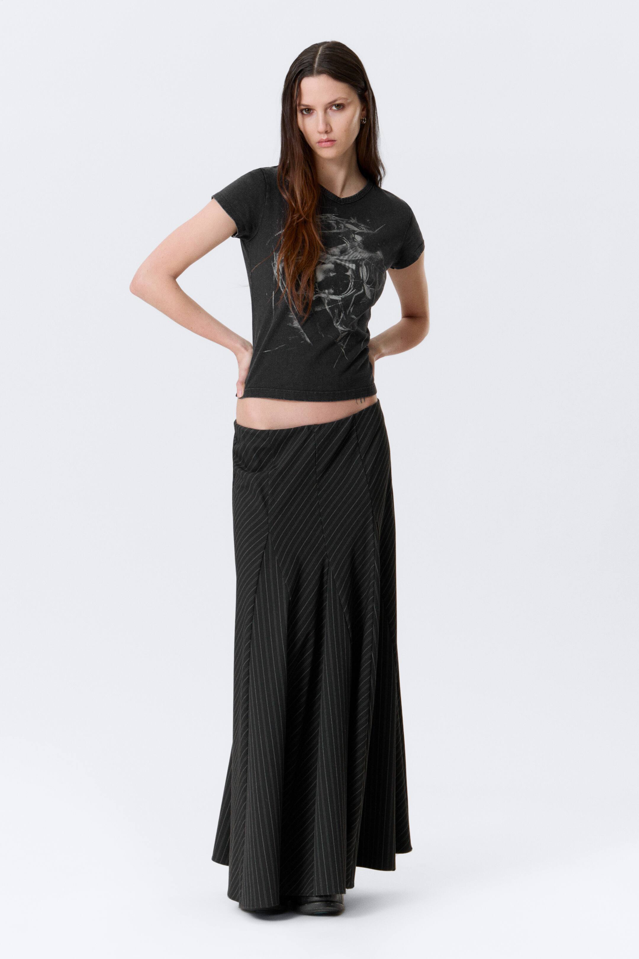 Agrandir l'image: La jupe longue noire à rayures fines présente une taille basse et une silhouette évasée, avec de fines rayures blanches courant verticalement et en diagonale sur des panneaux segmentés.