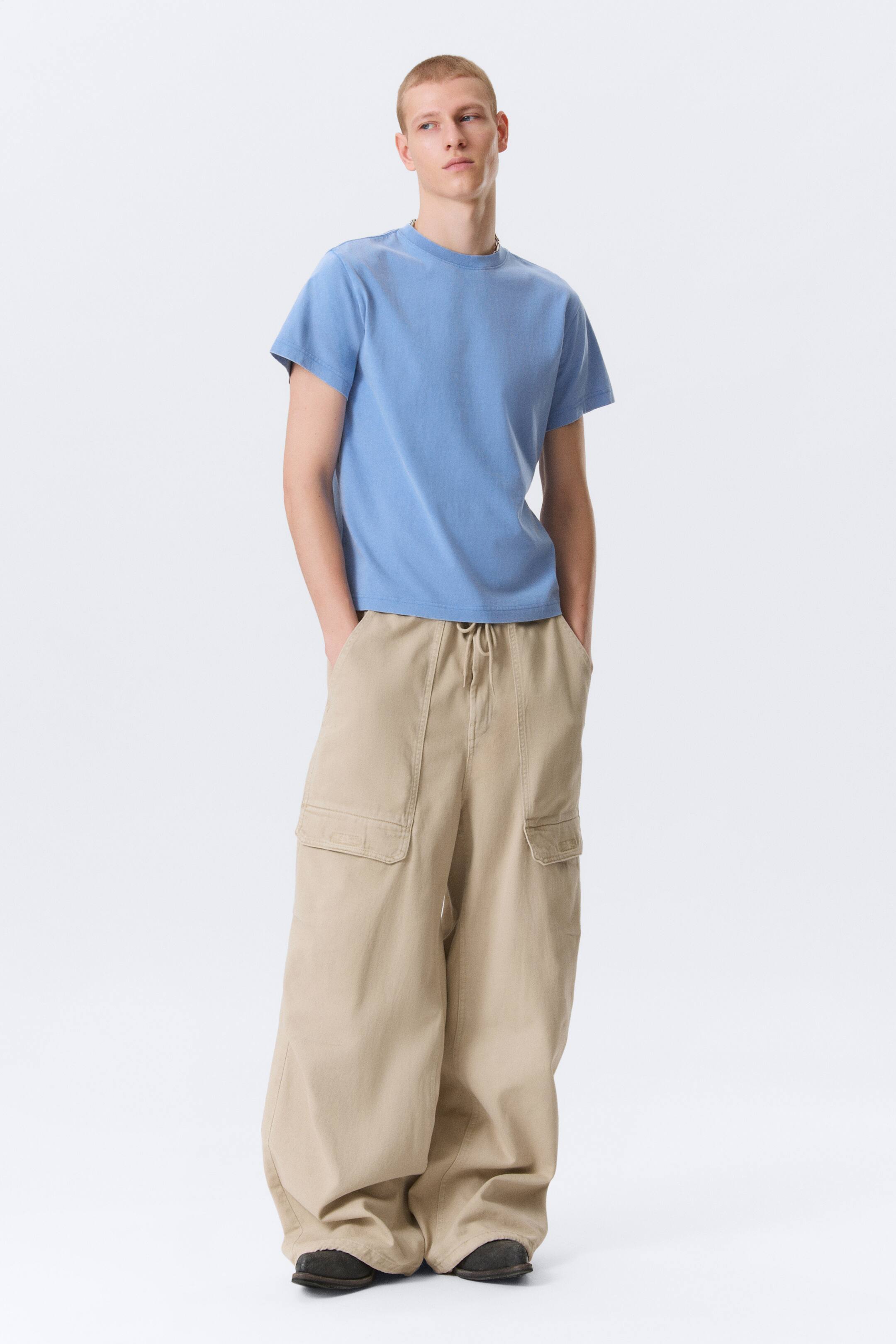 Agrandir l'image: Un t-shirt bleu clair à manches courtes et col rond est porté, offrant une coupe décontractée. Il est associé à un pantalon cargo beige à jambes larges, doté de grandes poches cargo à rabat sur les côtés et d'une taille à cordon de serrage.