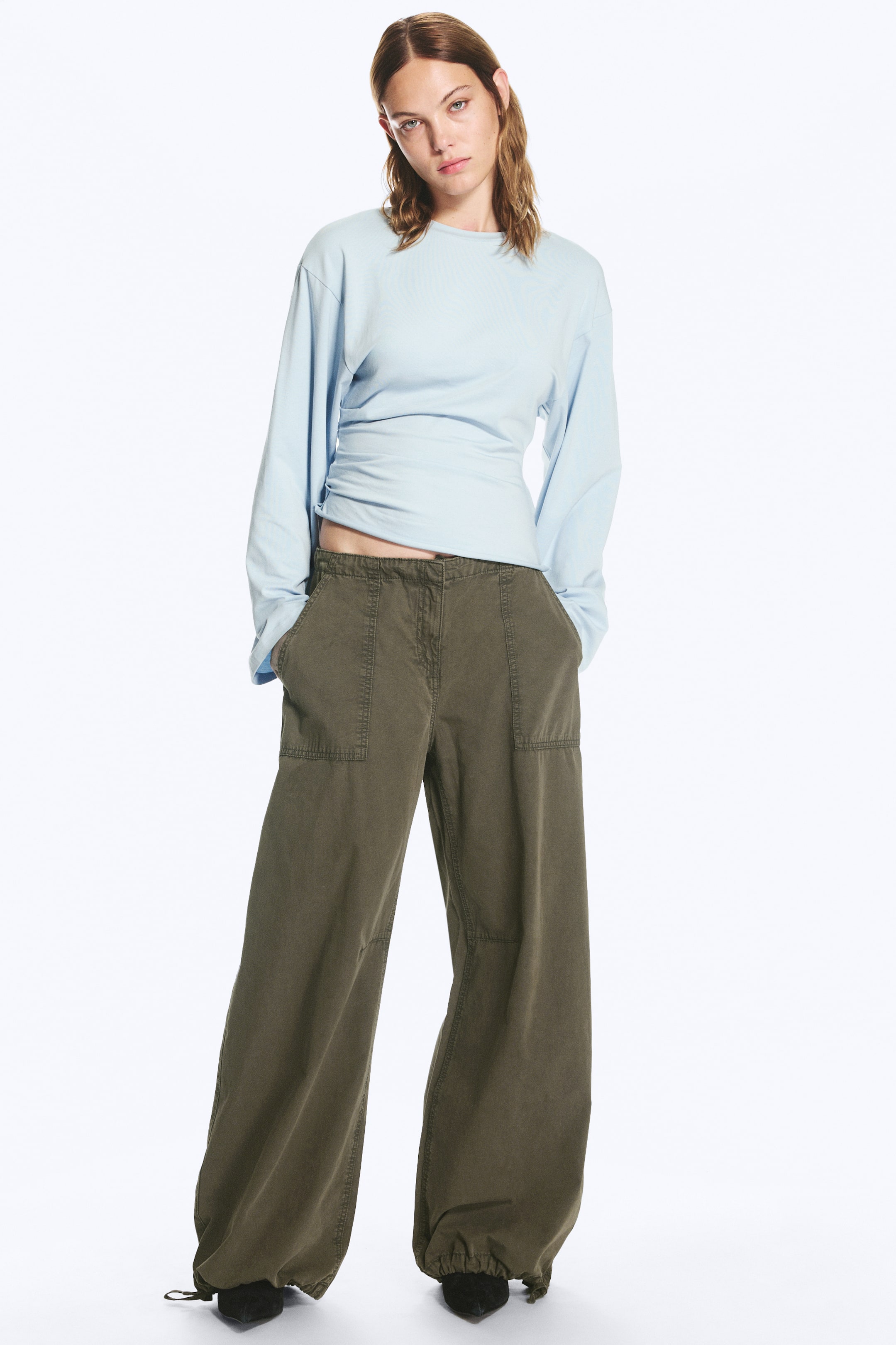 Visualizza l'immagine ingrandita: Pantaloni balloon con coulisse color verde oliva, caratterizzati da una silhouette a gamba larga e da tasche applicate frontali ben evidenti, indossati dalla modella. I pantaloni sono abbinati a un top azzurro a maniche lunghe e presentano orli con coulisse stretti alla caviglia.