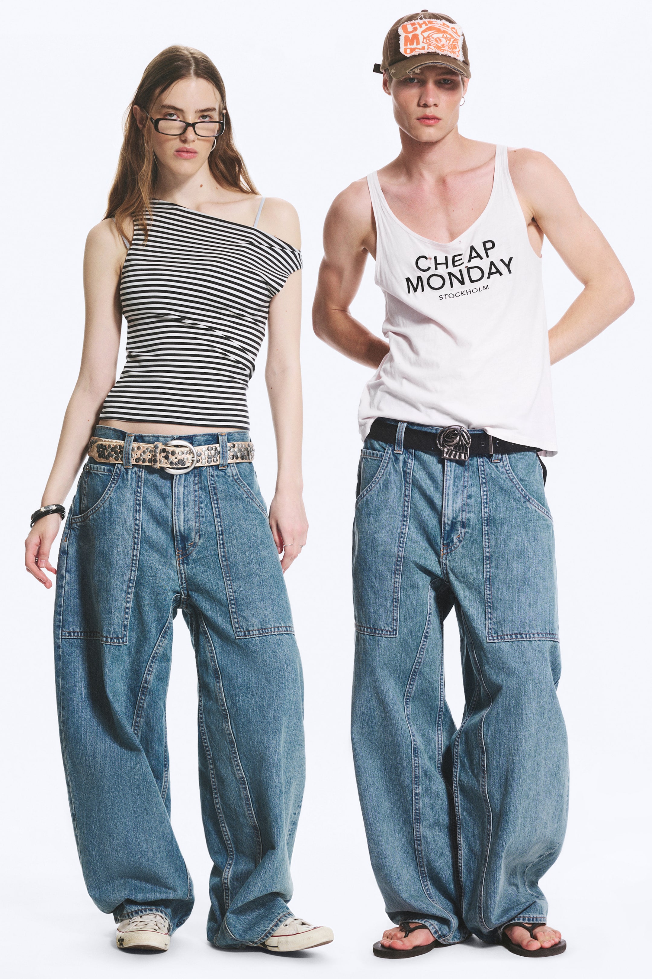 Agrandir l'image: Des jeans en denim à jambe large et délavage clair sont présentés sur deux modèles, tous deux de face, mettant en valeur leur coupe ample et décontractée. Les jeans se distinguent par des coutures frontales et latérales marquantes ainsi que de grandes poches plaquées rectangulaires sur les cuisses, stylisés avec des ceintures et des hauts décontractés.