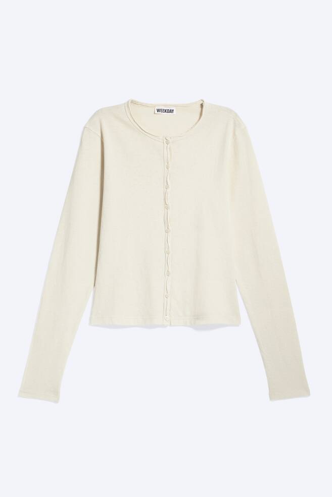Ein cremefarbener Cardigan wird von vorne gezeigt, mit einem Crewneck mit rohem Rand und einer durchgehenden Knopfleiste mit kleinen, runden cremefarbenen Knöpfen. Lange Ärmel sind sichtbar, und ein 'WEEKDAY'-Markenetikett ist am inneren Rückenkragen zu sehen. - 1