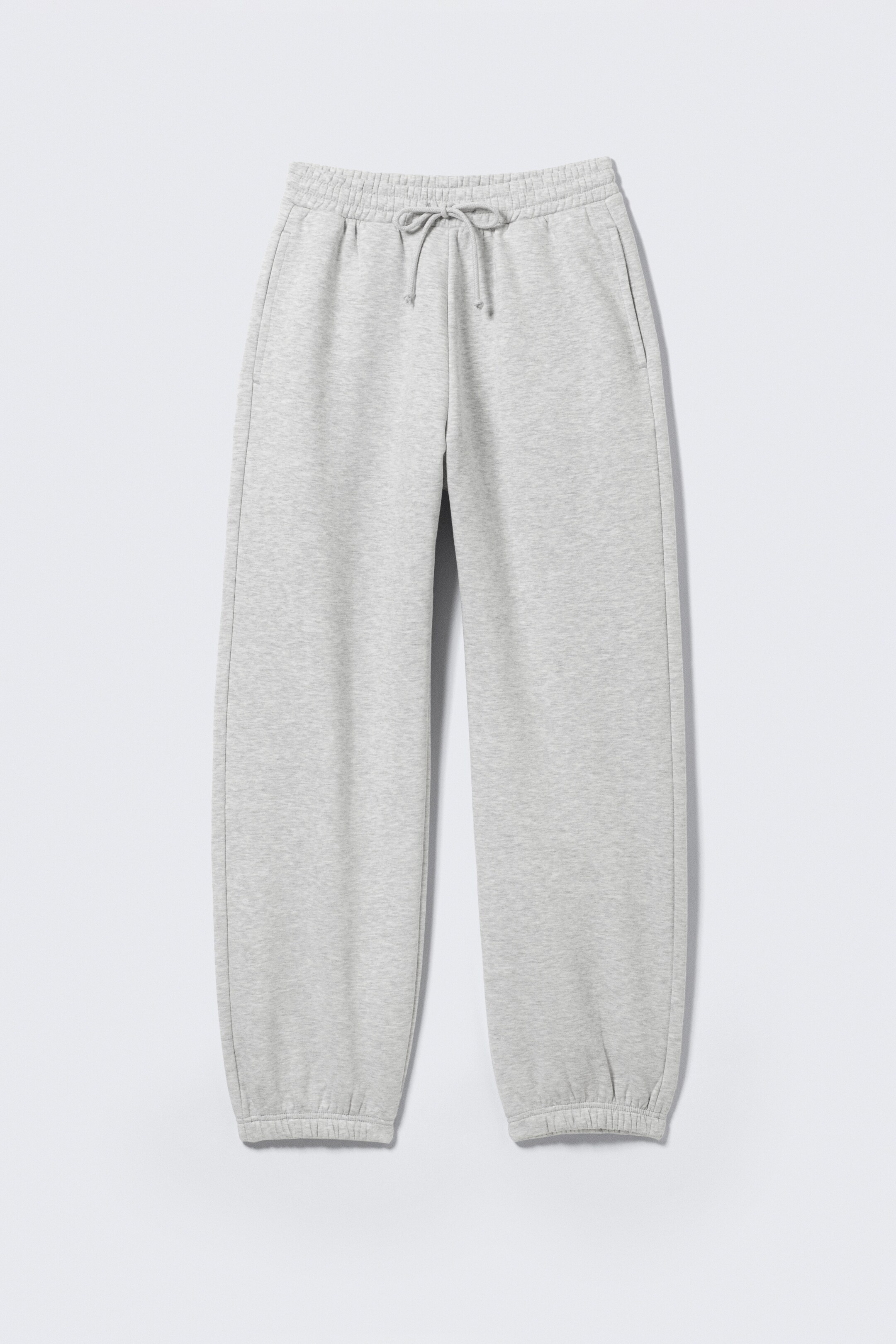 Agrandir l'image: Un pantalon de jogging en molleton de coton gris clair, présenté face avant en coupe régulière, est doté d'une taille élastiquée avec cordons visibles. Des poches latérales sont visibles sur chaque hanche, et les jambes se terminent par des poignets élastiqués.