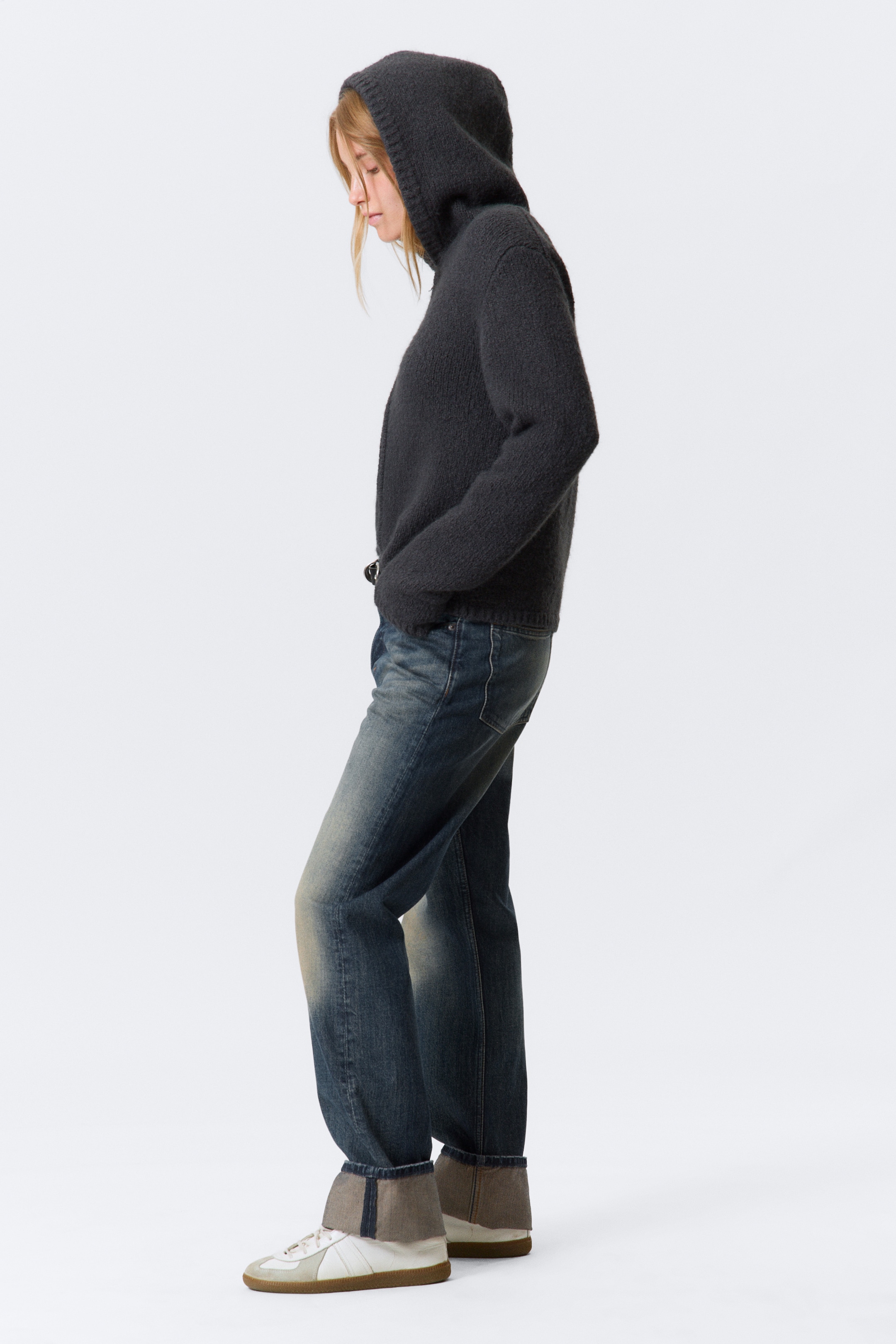 Visualizza immagine più grande: Un paio di jeans unisex a vita media con una vestibilità regolare e una gamba dritta, realizzati in denim rigido, è indossato dal modello. I jeans presentano un lavaggio scuro con sfumature più chiare sulle cosce e sulle ginocchia, e i loro orli sono ripiegati.