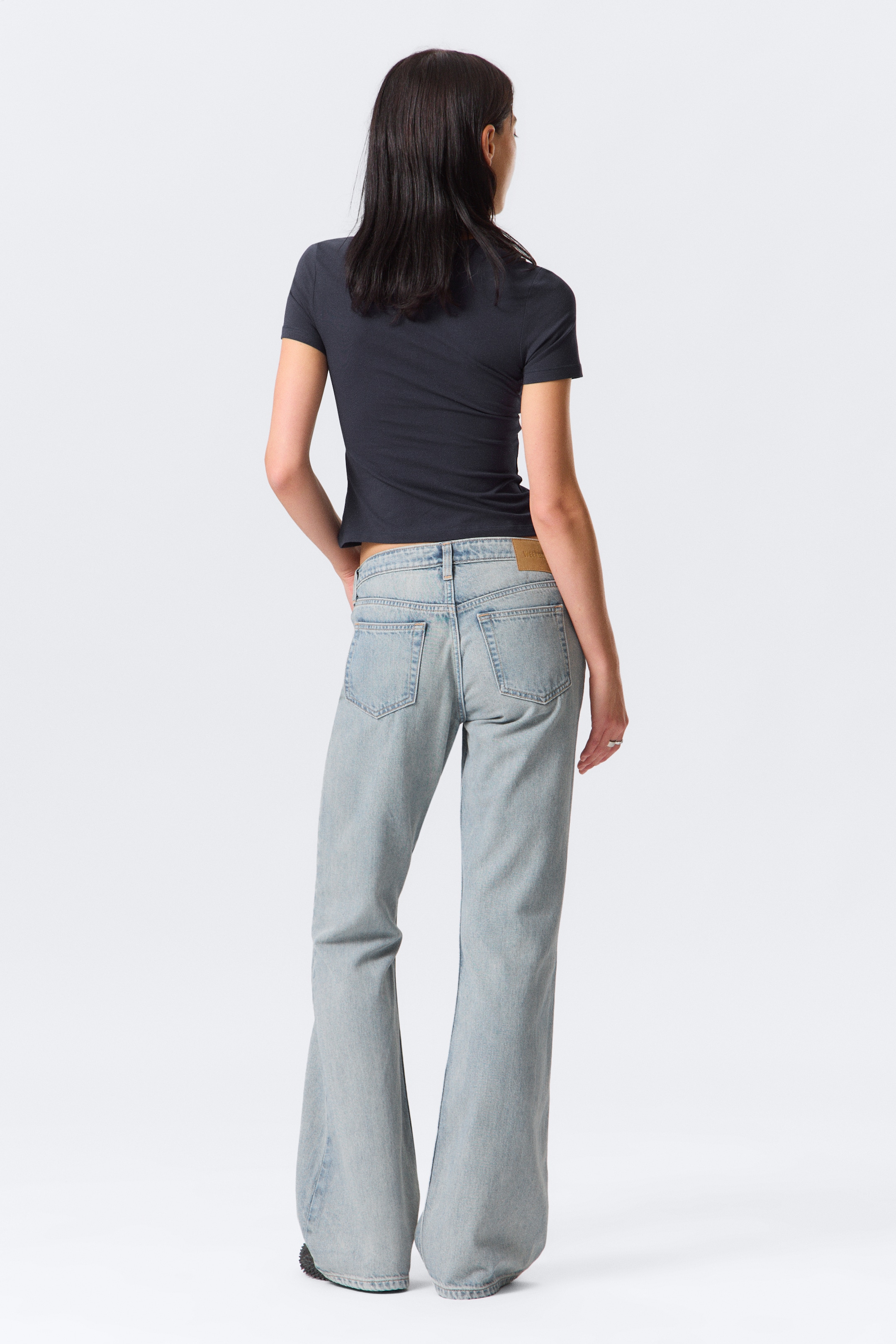 Visualizza immagine più grande: Jeans a vita bassa, slim-fit, bootcut in denim chiaro striato sono indossati da una modella. La lunghezza dei jeans si accumula ai piedi e la mano destra della modella è appoggiata in una tasca posteriore.