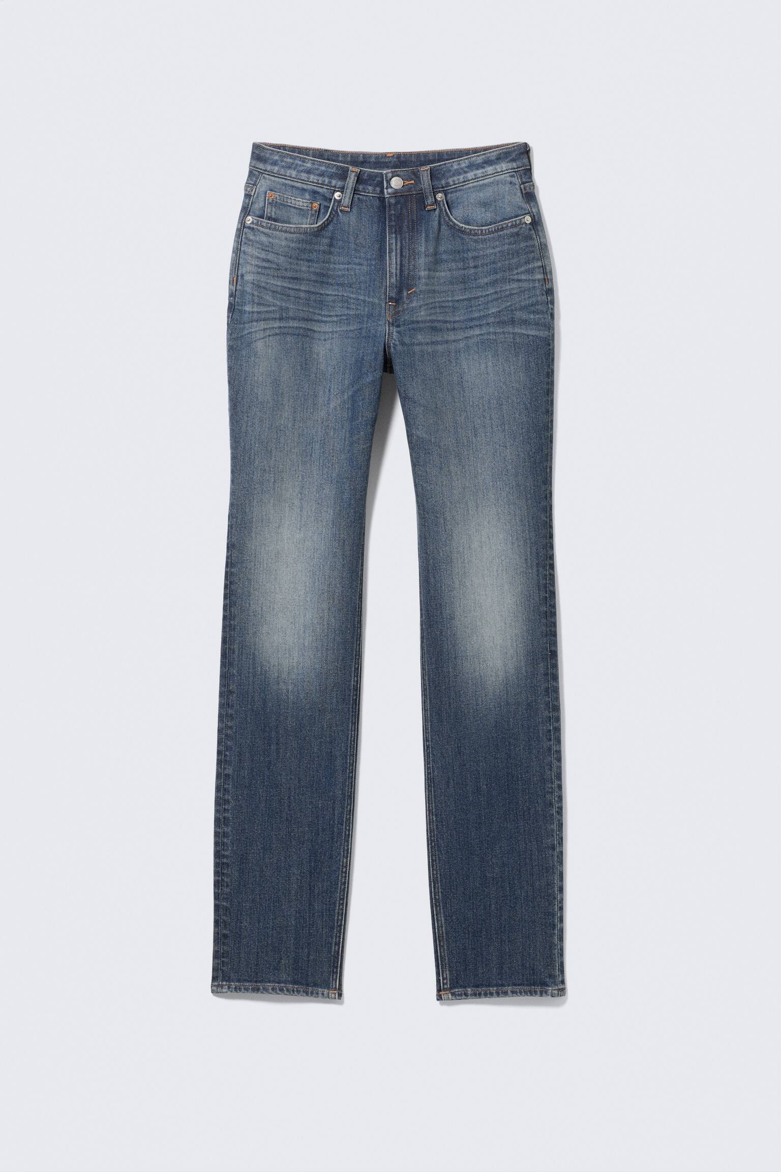 VOORaanzicht van blauwe denim jeans. De jeans tonen een vervaagde wassing met "whiskering" op de bovenbenen, een knoop- en ritssluiting, voorzakken en riemlussen.