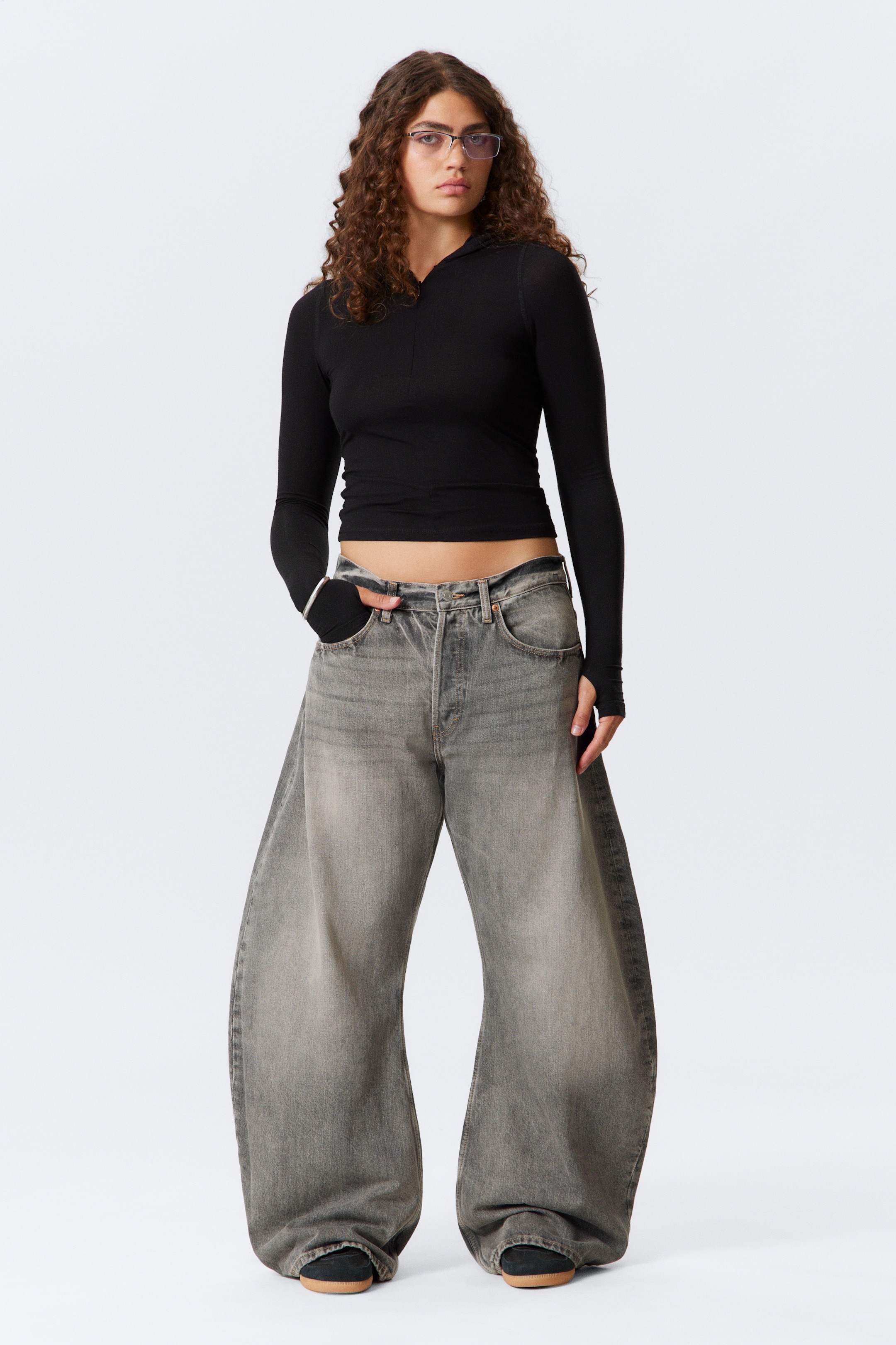 View larger image: A black semi-fitted long-sleeve hooded top, cropped to reveal the midriff, is featuring a quarter-zip neckline and thumbholes at the cuffs. It is styled with high-waisted, dark grey washed wide-leg jeans that are pooling at the ankles.