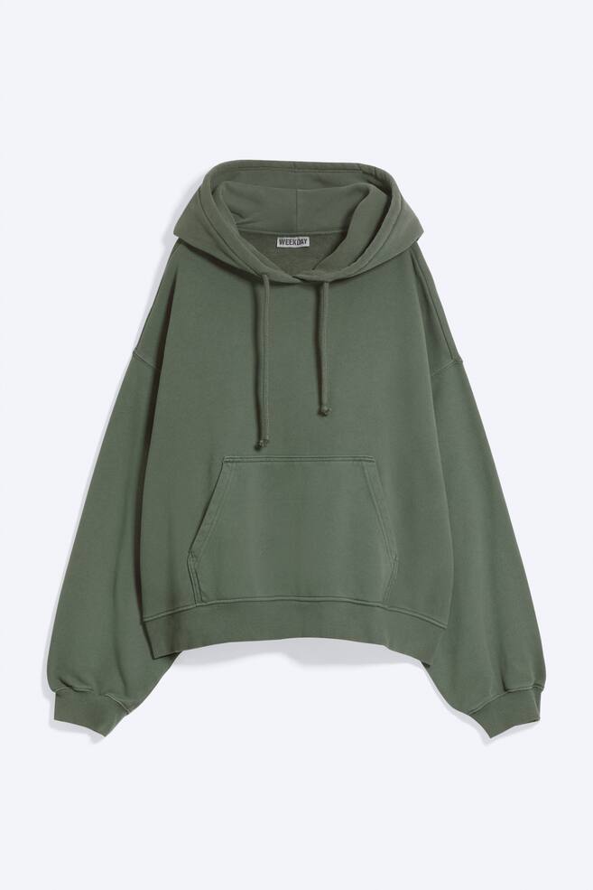 Una felpa con cappuccio verde salvia, vista frontalmente, presenta una vestibilitÃ  rilassata con spalle scese e maniche lunghe rifinite con polsini a costine. Il design mostra un cappuccio con coulisse regolabile, una tasca a marsupio frontale e un orlo a costine coordinato. - 1