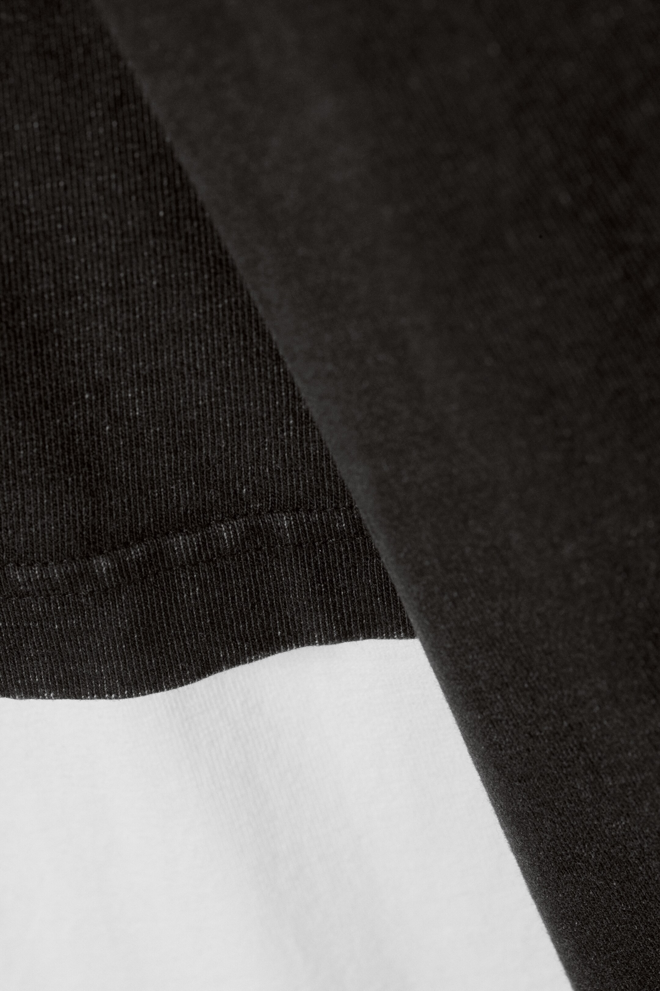 View larger image: A black fabric with a fine vertical texture and stitched hemline is layering over a smooth white fabric.