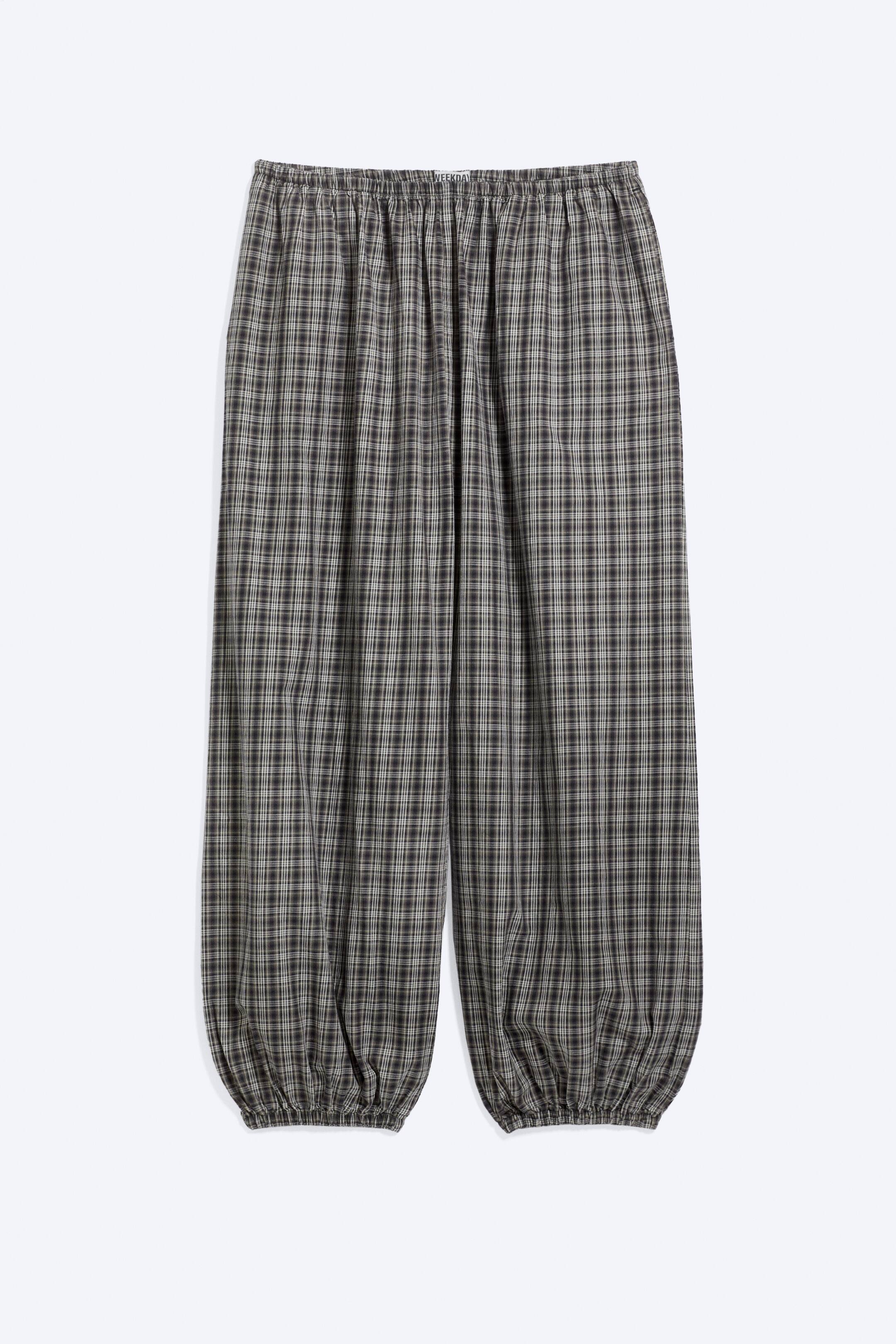 Größeres Bild anzeigen: Eine locker sitzende Karohose ist von vorne zu sehen und verfügt über einen gerafften elastischen Bund sowie elastische Beinabschlüsse an den Knöcheln, die eine ballonartige Silhouette erzeugen. Der Stoff zeigt durchgehend ein kariertes Muster in Dunkelgrau, Schwarz und Beige im entspannten Design.