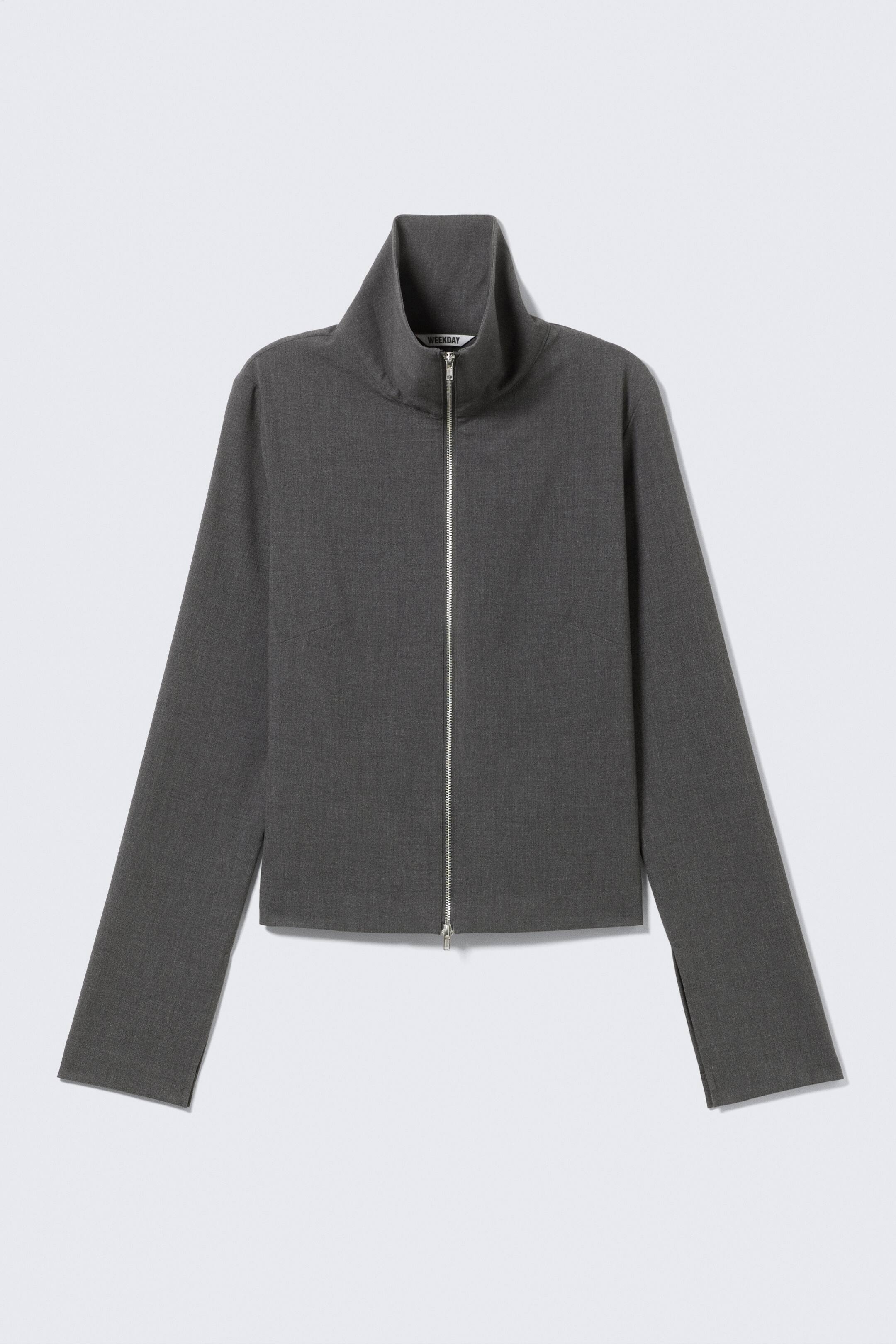 Grotere afbeelding bekijken: Een donkergrijs slim-fit shirt met lange mouwen wordt getoond (FRONT), vervaardigd uit kostuumstof en voorzien van een hoge, dubbelgelaagde kraag. Een zilverkleurige tweerichtingsrits loopt middenvoor; vormgevende darts zijn zichtbaar aan de zijkanten en er zijn subtiele splitjes in de omgeslagen mouwzomen, terwijl de onderzoom eveneens omgeslagen en scherp afgewerkt is.