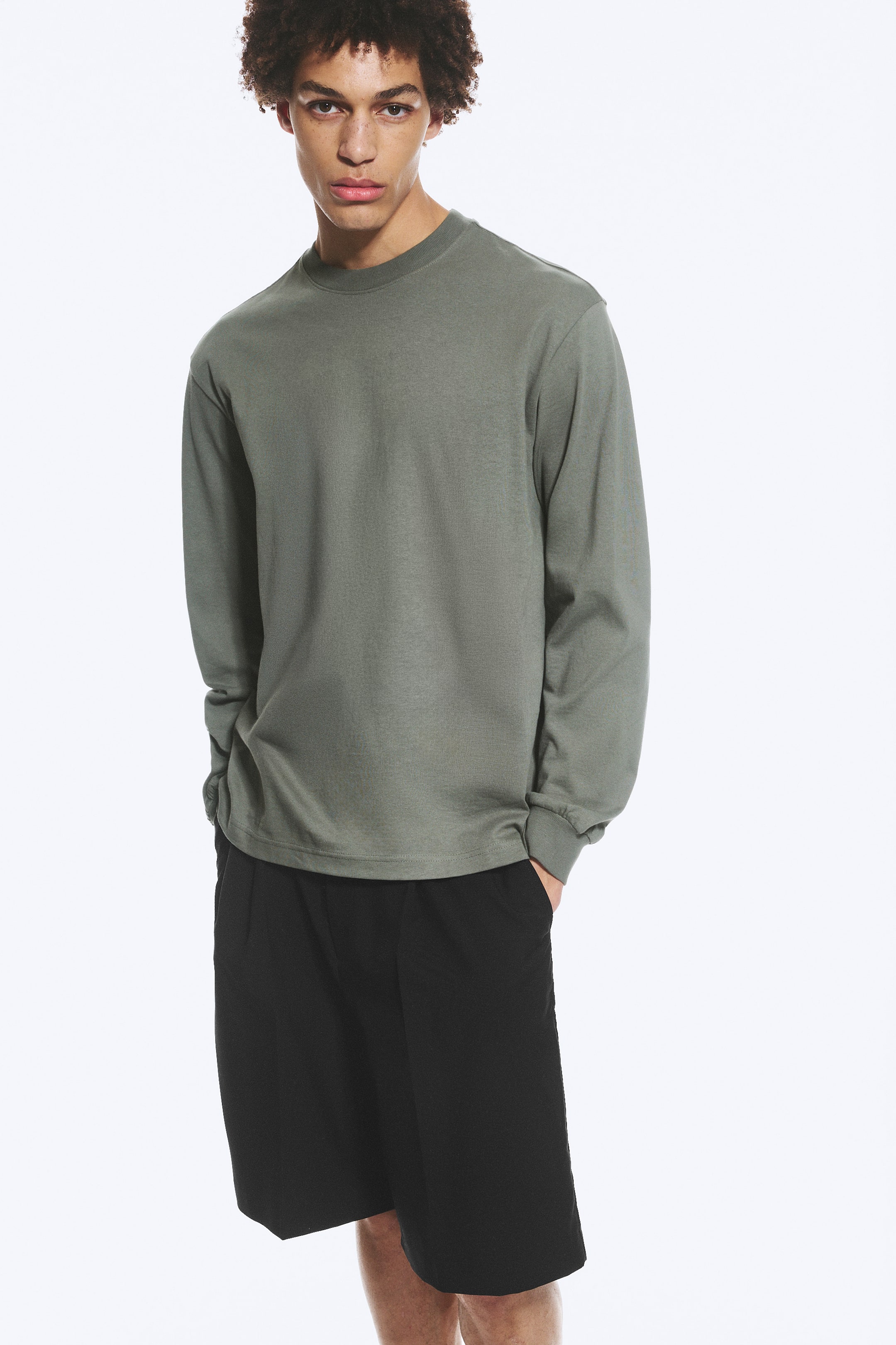 Visa större bild: En olivgrön långärmad t-shirt presenteras, med rund hals och ribbade muddar. Den är löst sittande och är stylad över svarta shorts.