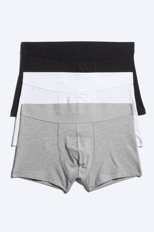 A three-pack of boxer trunks is shown presenting three pairs in black, white and grey, arranged in an overlapping stack facing the front. Each pair features a wide, tonal elastic waistband and a contoured front pouch with vertical stitching. - 1