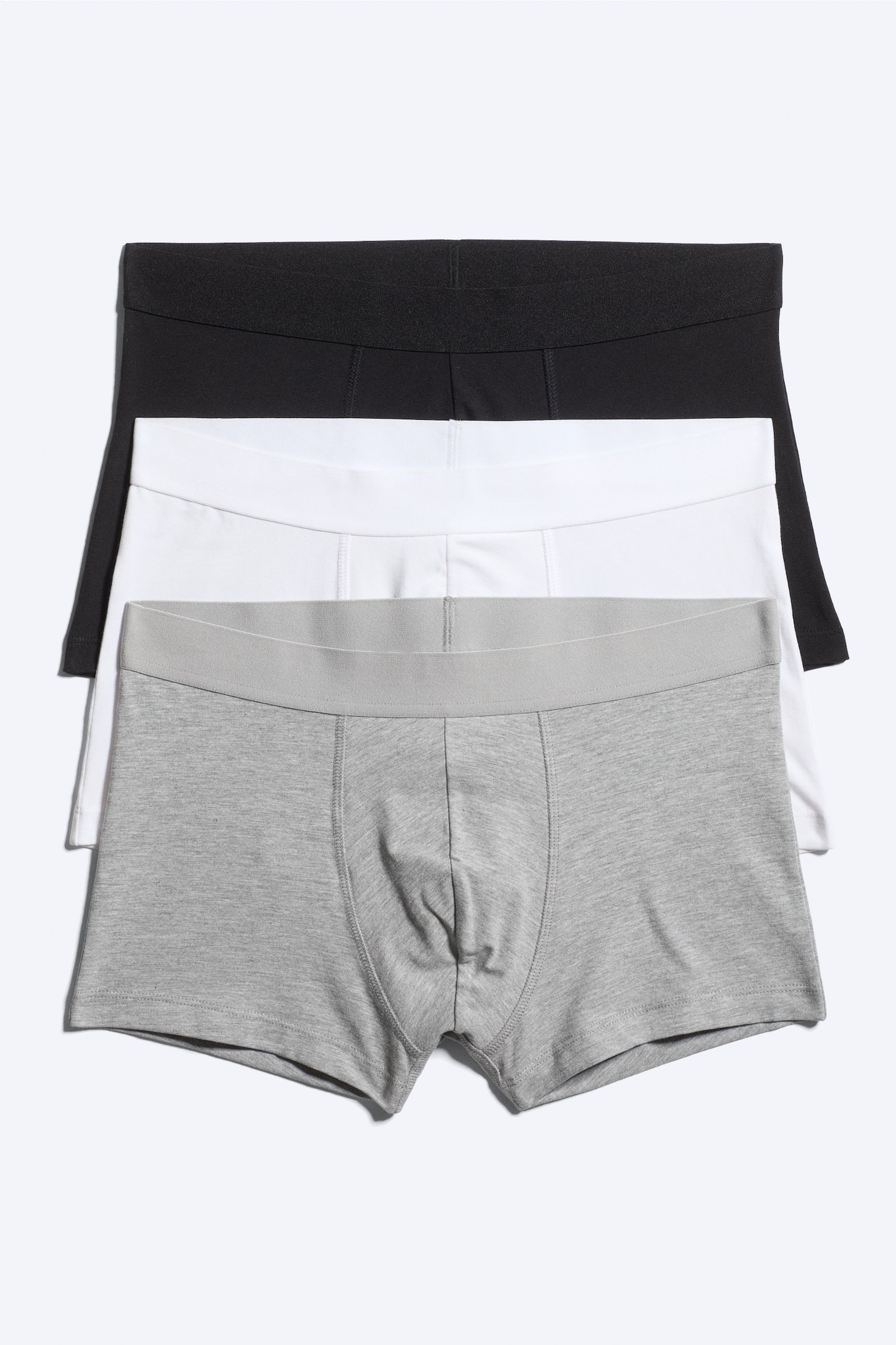 Ett trepack boxer briefs visar tre par i svart, vitt och grått, arrangerade i en överlappande stapel vända mot framsidan. Varje par har en bred, ton-i-ton resårmidja och en formad frontficka med vertikala sömmar.