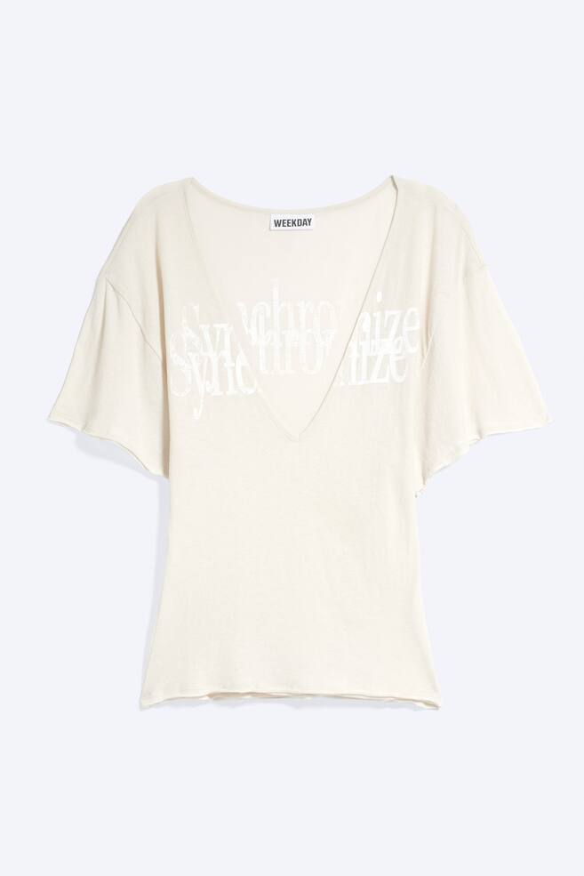 Ein cremefarbenes T-Shirt ist von vorne zu sehen und verfÃ¼gt Ã¼ber einen tiefen V-Ausschnitt, locker geschnittene kurze Ãrmel und SÃ¤ume mit offener Kante. Ãber den Brustbereich des Shirts verlÃ¤uft ein weiÃer Grafikdruck. - 1