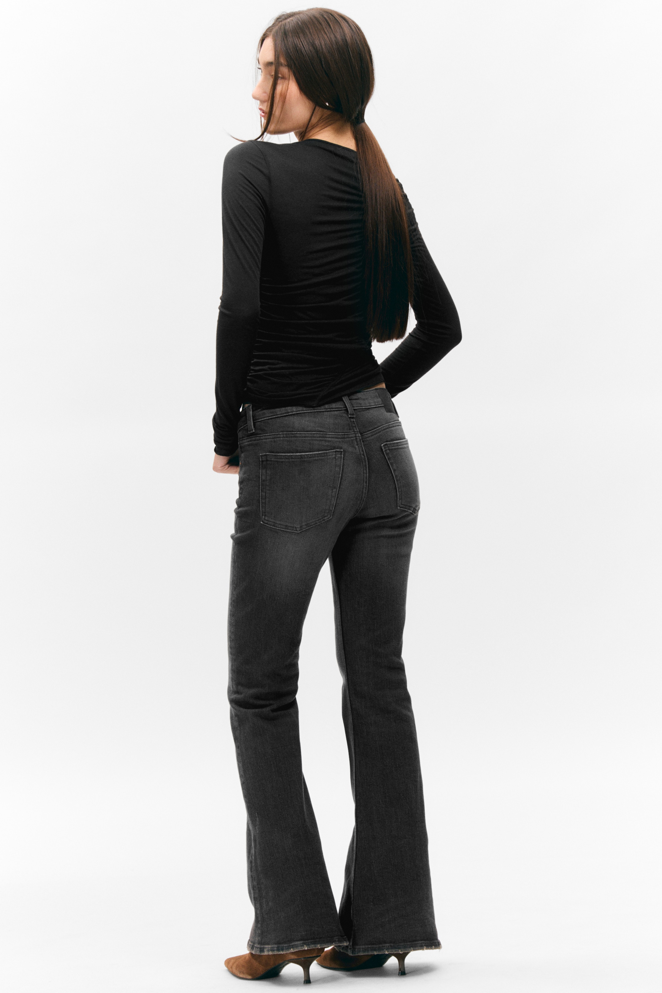 Visualizza immagine più grande: Un top nero a maniche lunghe con arricciature raccolte lungo la schiena e i lati è indossato dalla modella. Il top ha una vestibilità aderente ed è abbinato a jeans lavaggio scuro.