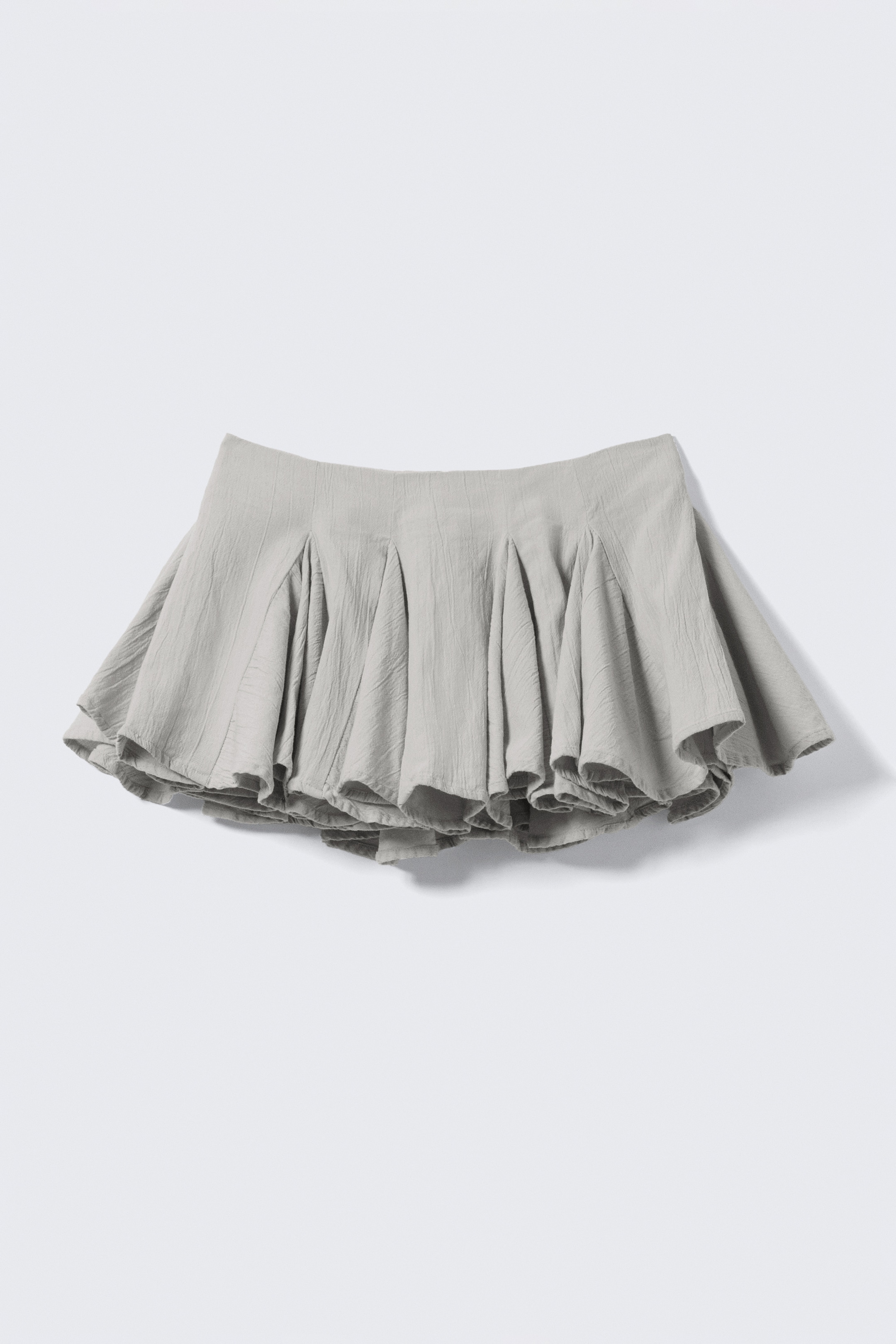Agrandir l'image: Une mini-jupe gris clair est présentée de FACE, avec une ceinture lisse. Elle affiche une silhouette plissée volumineuse avec une forme évasée et une structure subtile dans son tissu texturé.