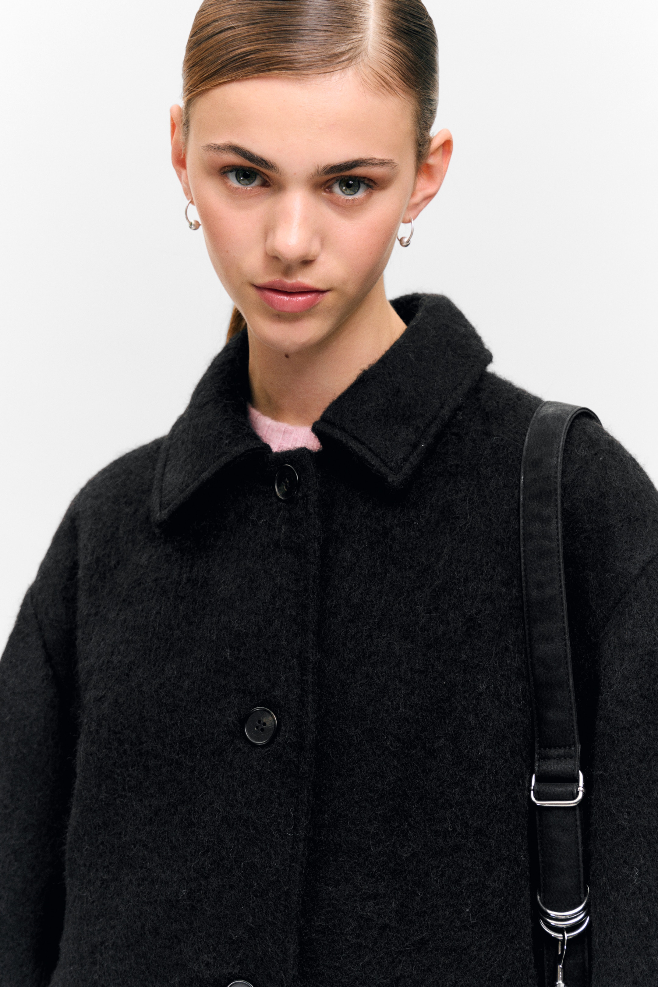 View larger image: A black fuzzy coat is being worn, featuring a classic collar and dark buttons down the front. A pink top is visible underneath, and a black bag strap is resting on the shoulder.