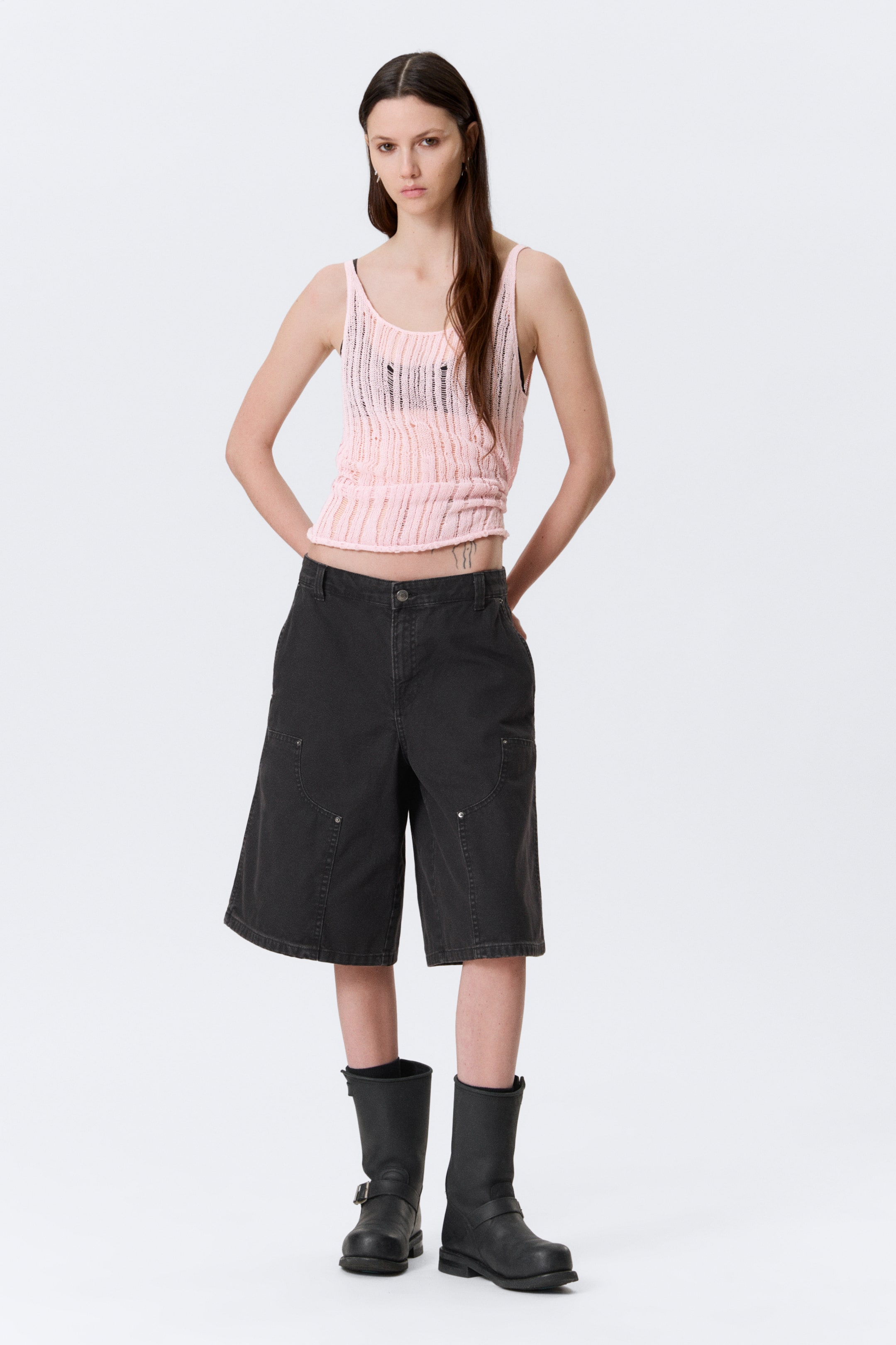 Zobrazit větší obrázek: Vyšisované černé cargo šortky se vyznačují uvolněným střihem s širokými nohavicemi, které sahají těsně nad kolena. Mají zapínání na knoflík a zip vpředu, boční kapsy a dvě velké stehenní cargo kapsy, z nichž každá má zakřivené švy a dva kovové nýty.