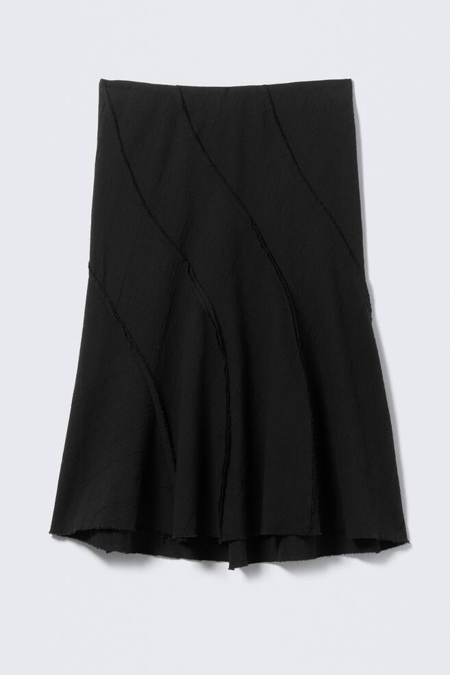 The black skirt features a crinkled texture and diagonal, raw-edged seams across its front. It flares towards an unfinished hem. - 1