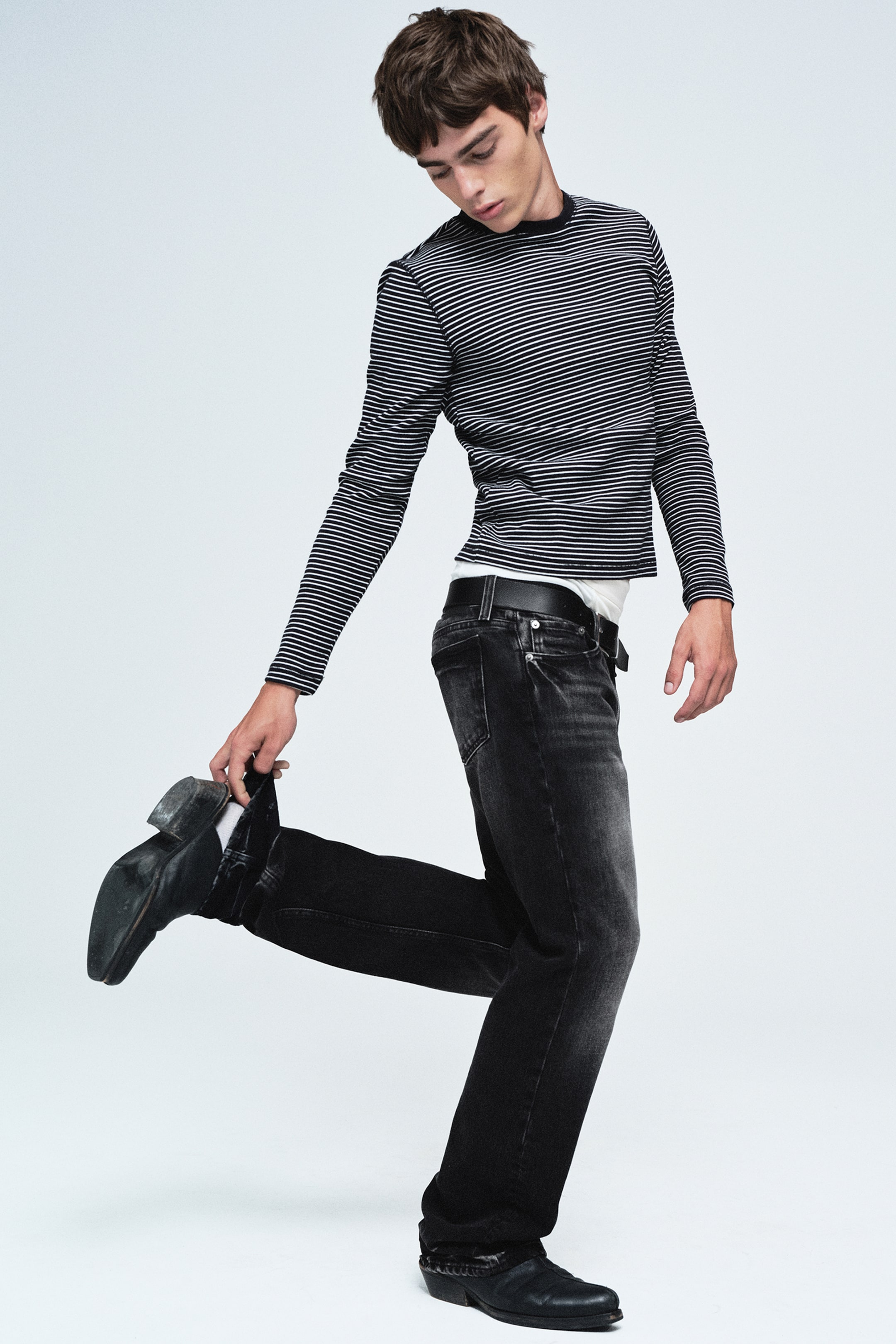 Se større billede: Sky low-rise regular bootcut-jeans i en falmet sort vask vises fra en sideprofil, hvilket fremhæver deres lavtaljede talje og klassiske femlommers konstruktion. Jeansene har en regular fit, der går over i et diskret bootcut-ben og falder ned over sorte støvler.