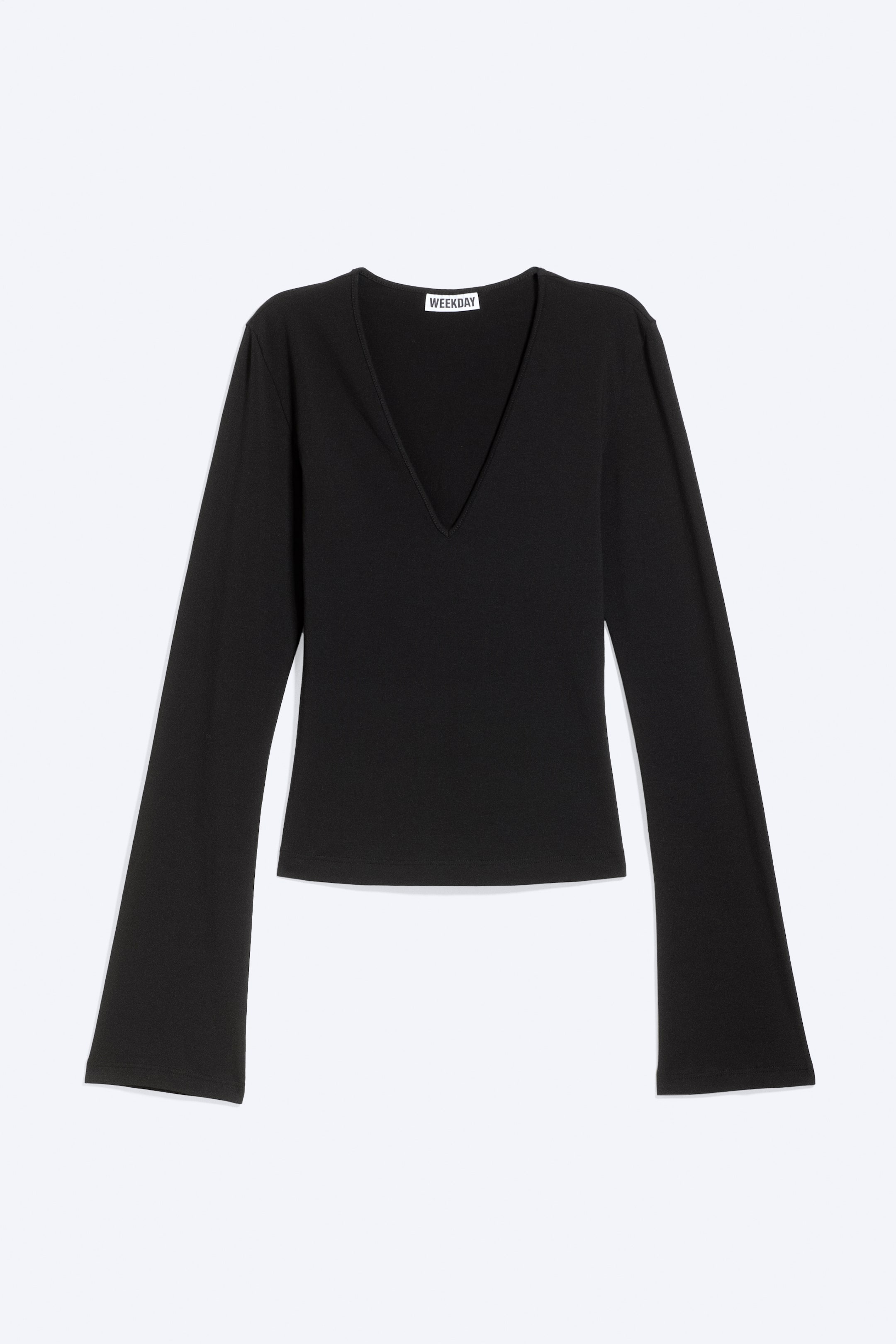 Ver imagen más grande: Una blusa negra de manga larga vista de frente, con un escote en pico profundo y mangas acampanadas. La prenda también presenta una sutil textura acanalada, un bajo recto y una etiqueta de la marca "WEEKDAY" en el escote.