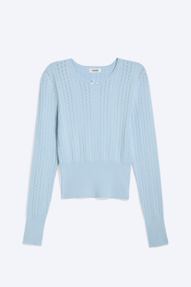 Hellblauer Strickpullover wird von vorne präsentiert, mit Rundhalsausschnitt und langen Ärmeln. Er zeigt vertikale Rippmuster mit Ösendetails über den gesamten Körper und die Ärmel, eine kleine Schleife am mittleren Ausschnitt sowie einen gerippten Saum und Bündchen. - 1