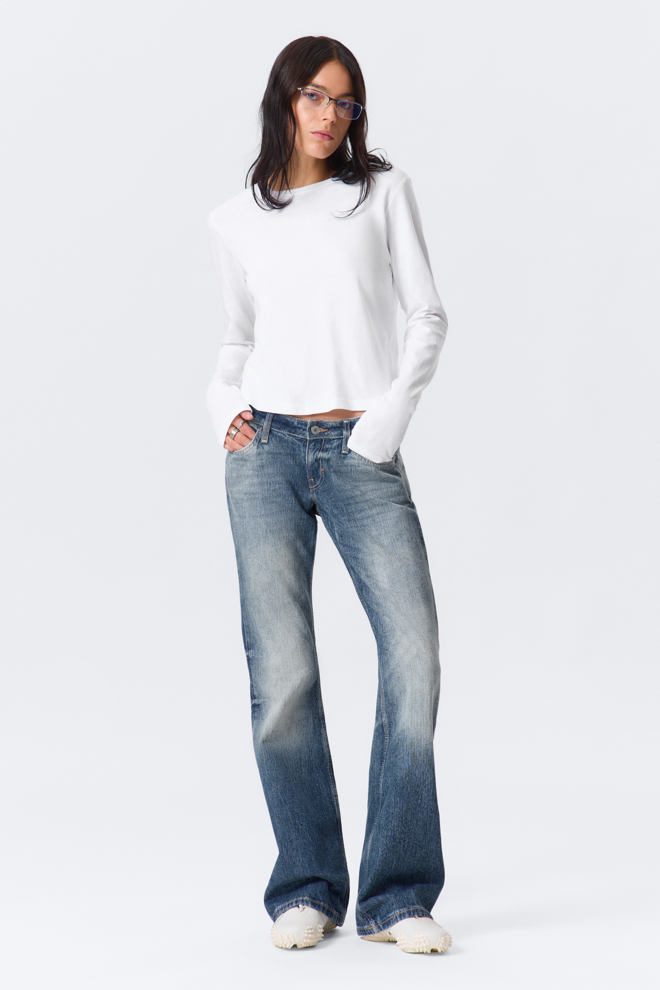 View larger image: A white long-sleeved top with a crew neckline and a straight hem is being worn by the model. The top features a slim fit, and its long sleeves are extending over the model's hands, which are placed in the pockets of blue jeans.