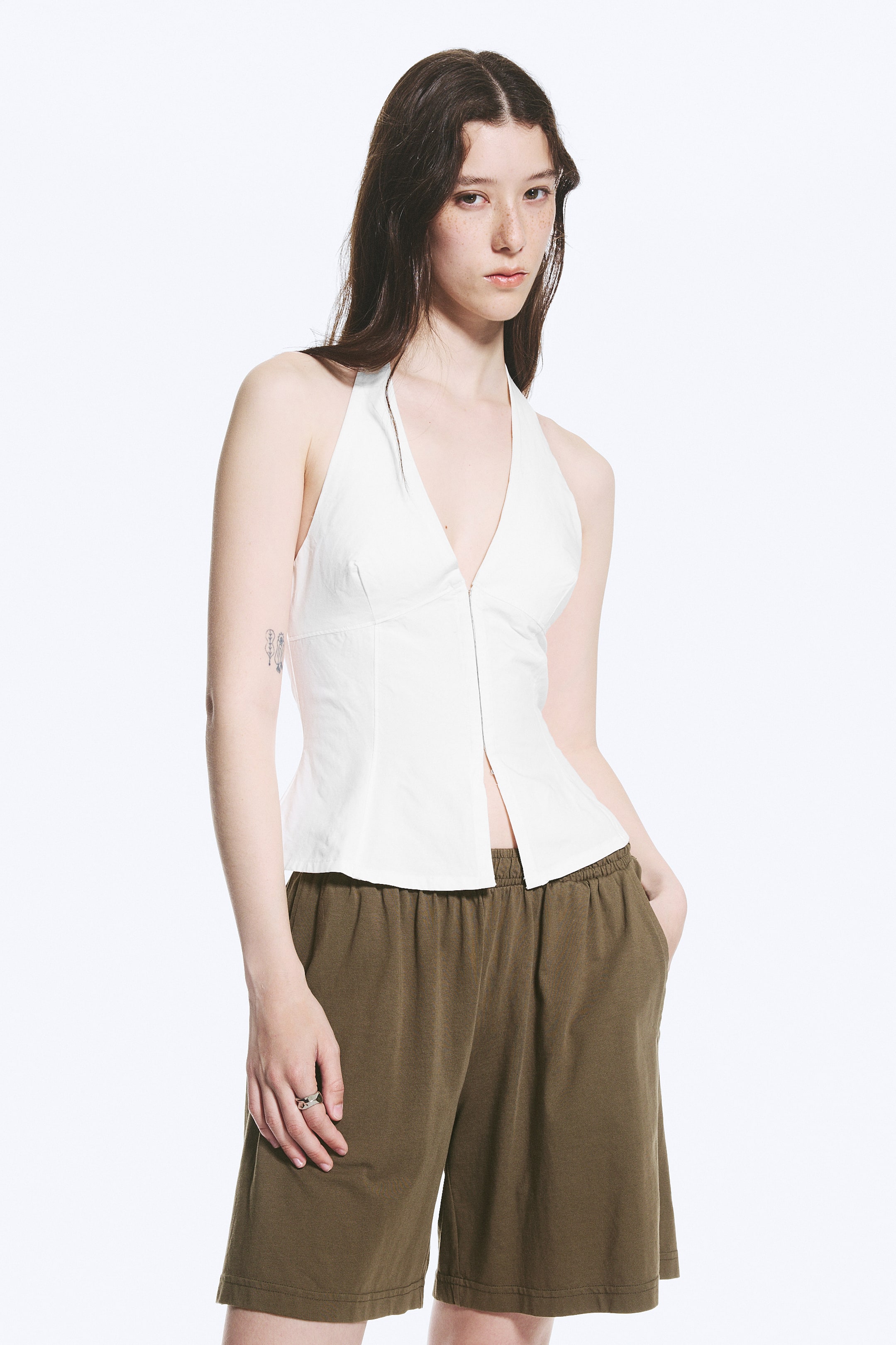 Se større billede: En hvid haltertop med dyb V-udskæring og en tætsiddende overdel med formende sømme, der præsenterer en midterfront knapstolpe og en lige kant.