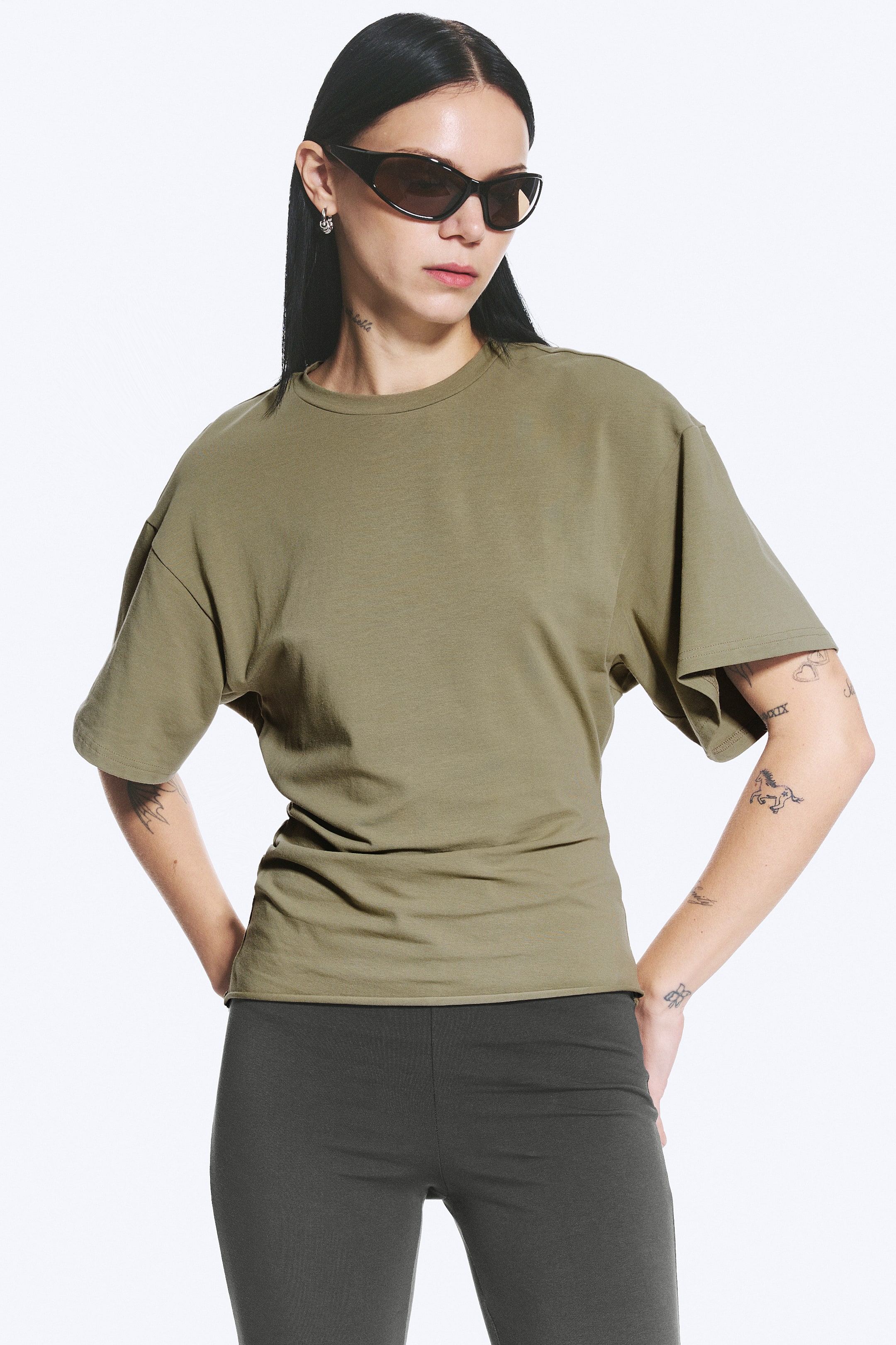 View larger image: An olive green t-shirt is displayed from a front-facing angle, featuring a classic crew neck and short, wide sleeves with dropped shoulders. It showcases a relaxed, oversized fit that tapers to a fitted hem.