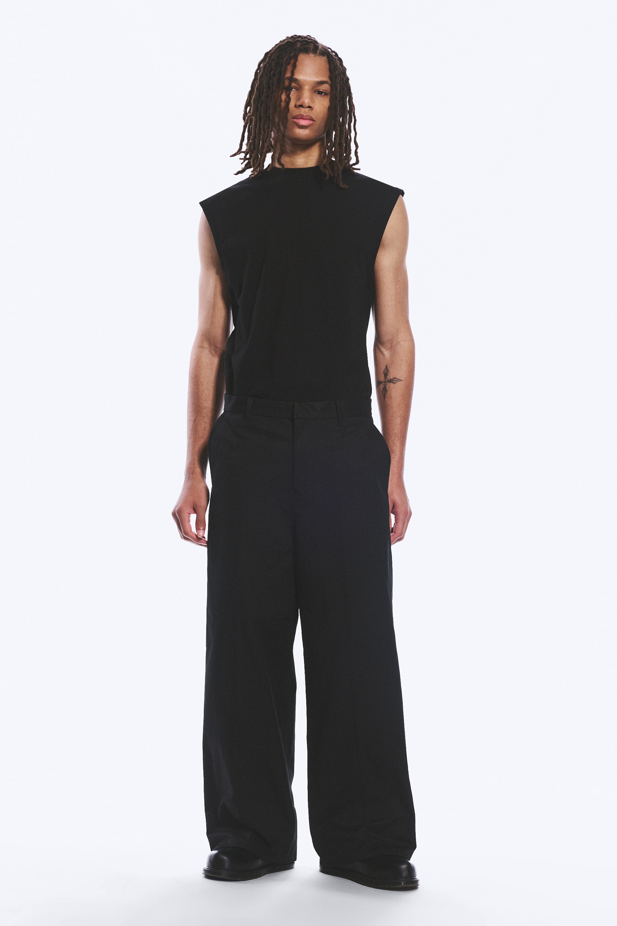 Ver imagem maior: Um top preto sem mangas com gola alta e corte descontraído, usado por dentro de umas calças pretas de perna larga. As calças apresentam uma frente lisa e um comprimento total com um corte descontraído.