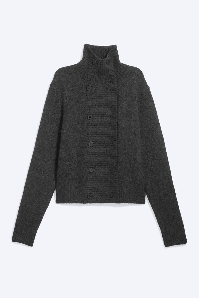 Uma camisola de malha cardigÃ£ cinzento-escuro, com duplo abotoamento, estÃ¡ virada para a frente, apresentando gola alta canelada e um amplo painel central canelado com duas colunas paralelas de botÃµes escuros. A camisola de malha destaca mangas compridas com punhos canelados e uma bainha direita canelada. - 1